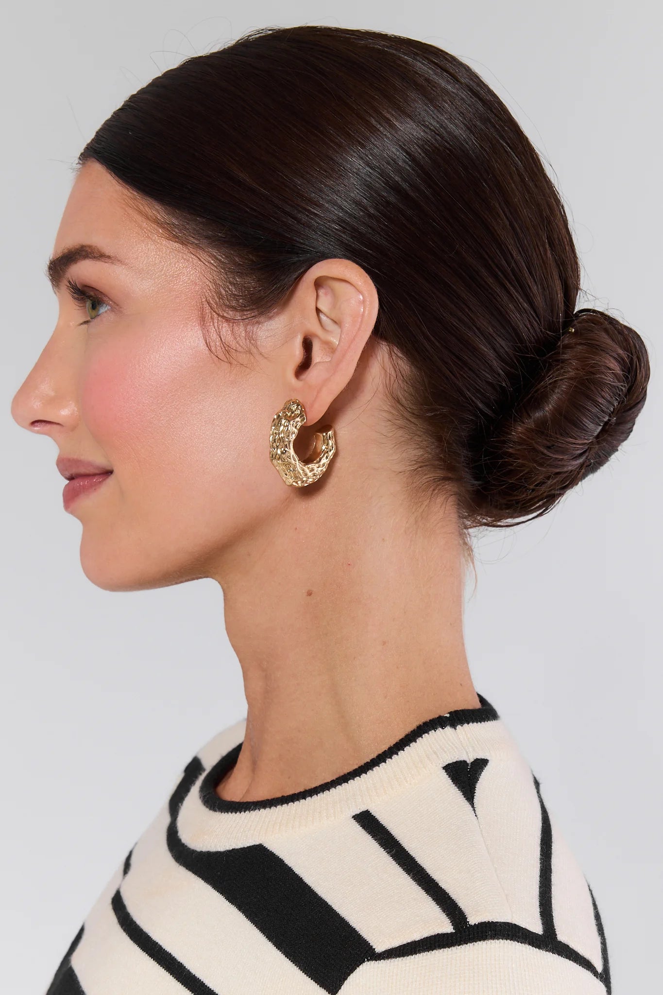 Woman with a styled bun wearing gold hoop earrings against a neutral background
