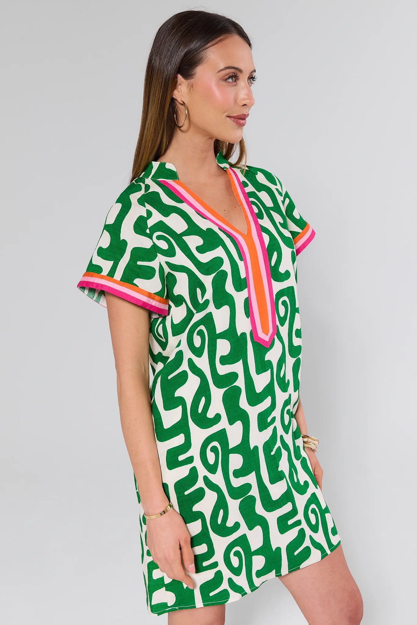Woman wearing a green patterned dress with colorful trim on a plain background