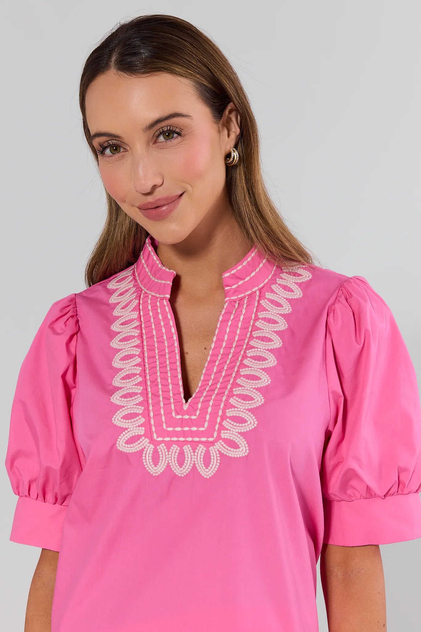 close up Woman wearing a pink blouse with white embroidery on a plain background