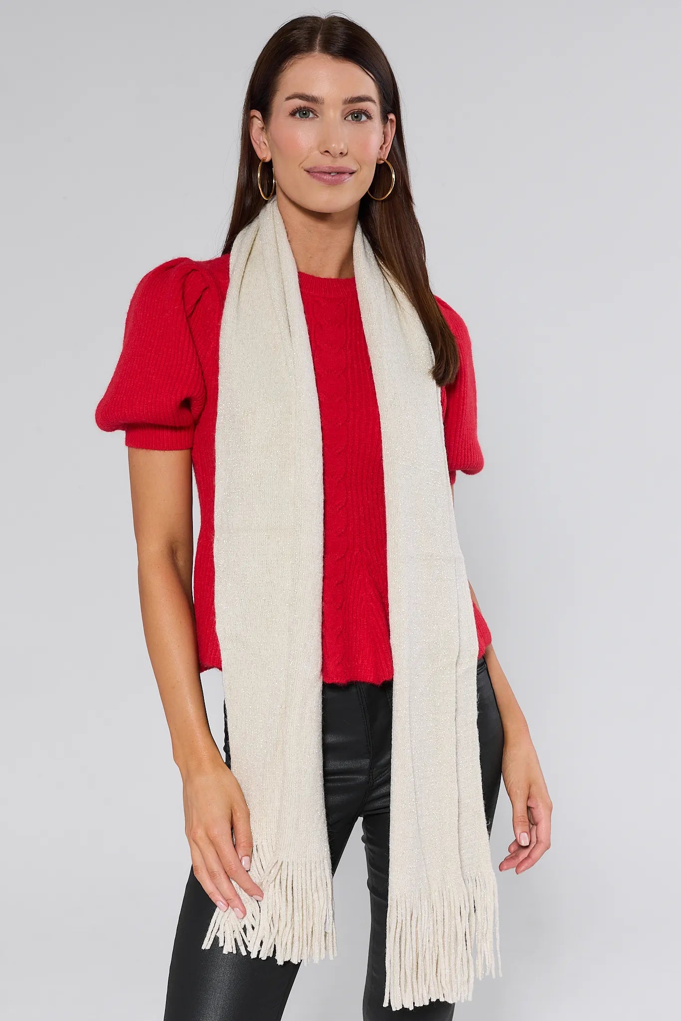Woman wearing a red top and black pants with a long Karris Cream Fringe Scarf on a plain background