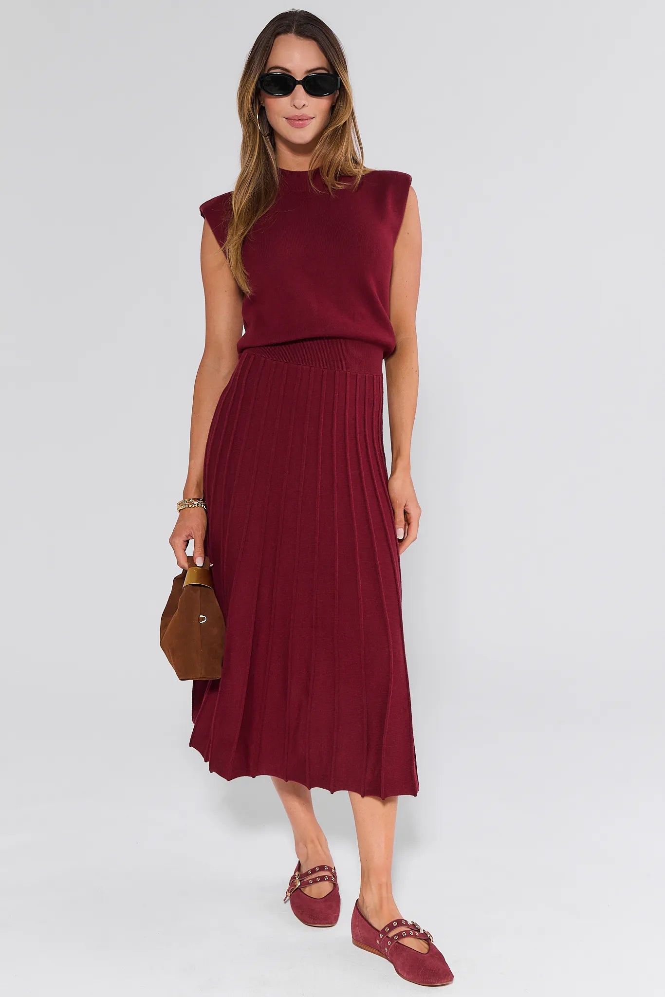Woman wearing a burgundy sleeveless Josie Dress with sunglasses and a brown handbag on a white background