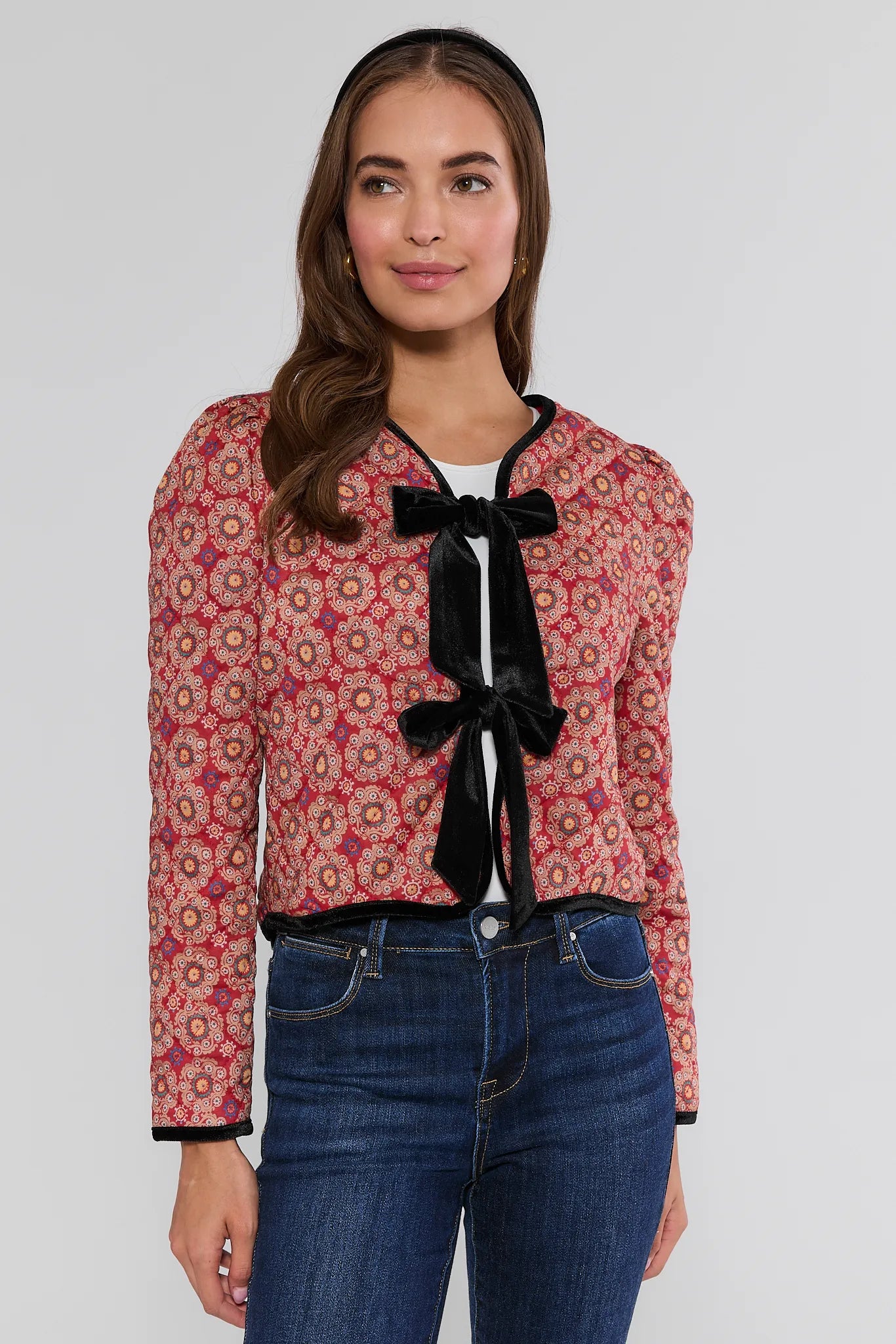 Woman wearing a patterned Ember Jacket with a black bow and jeans on a white background