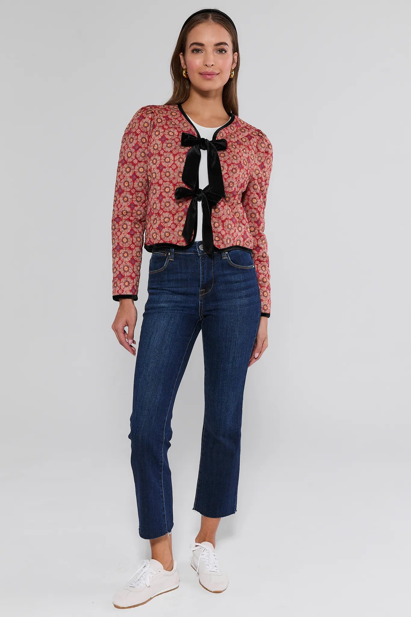 Woman wearing a red patterned Ember Jacket with a bow tie and blue jeans on a white background
