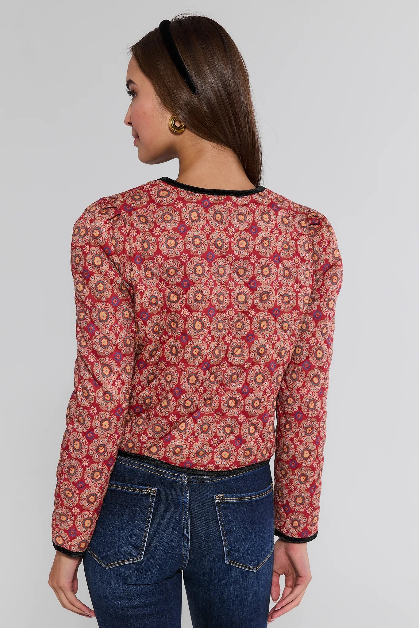 Woman wearing a red floral Ember Jacket and blue jeans on a plain background