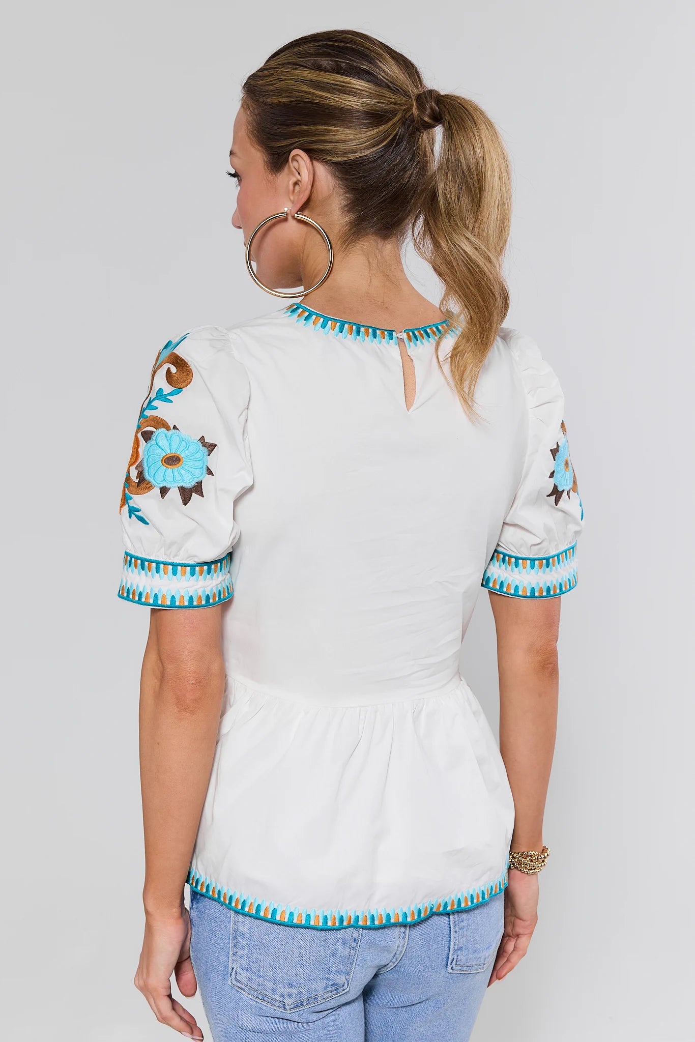 Woman wearing a white blouse with colorful embroidery on a plain background