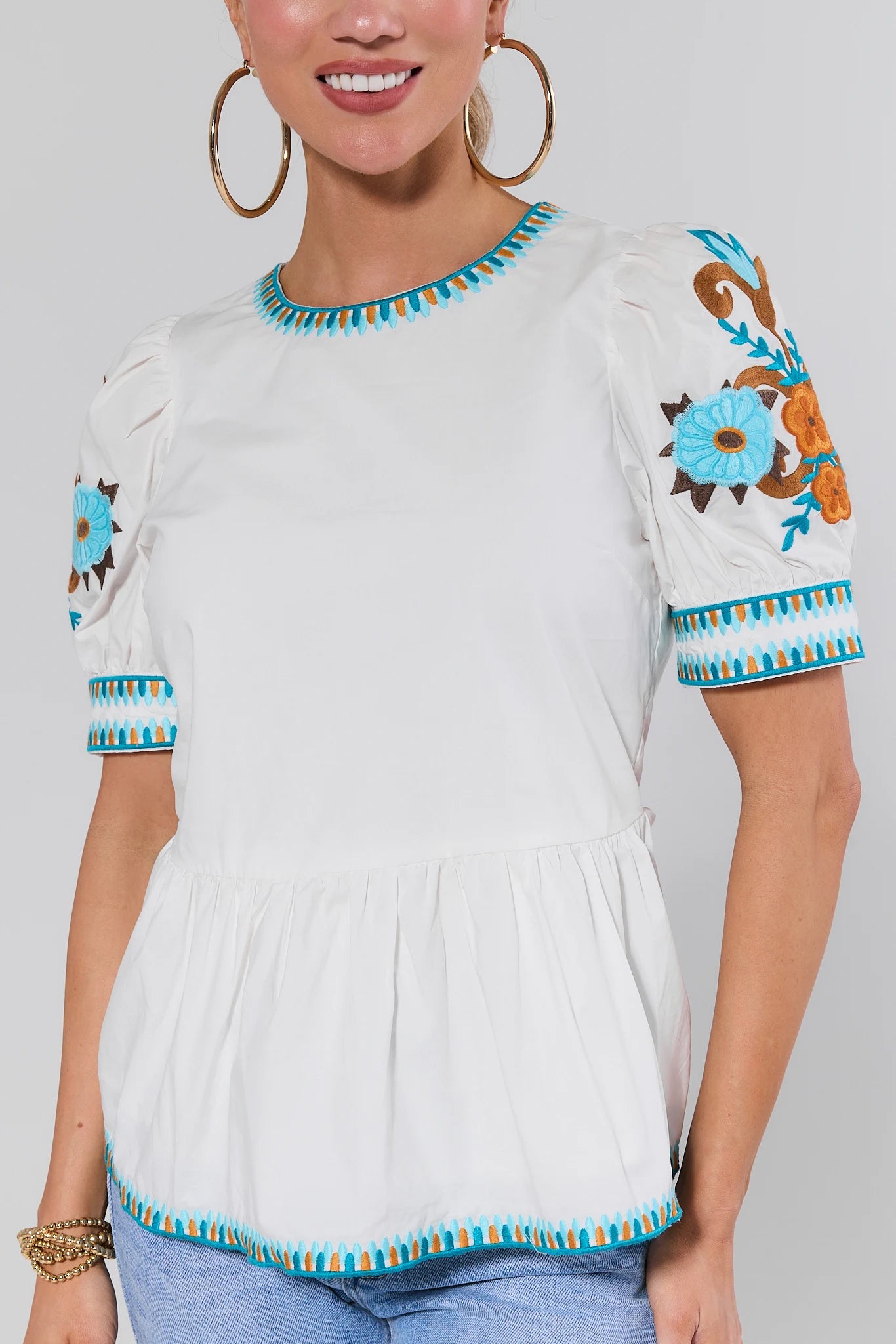 Person wearing a white blouse with colorful embroidery on a plain background