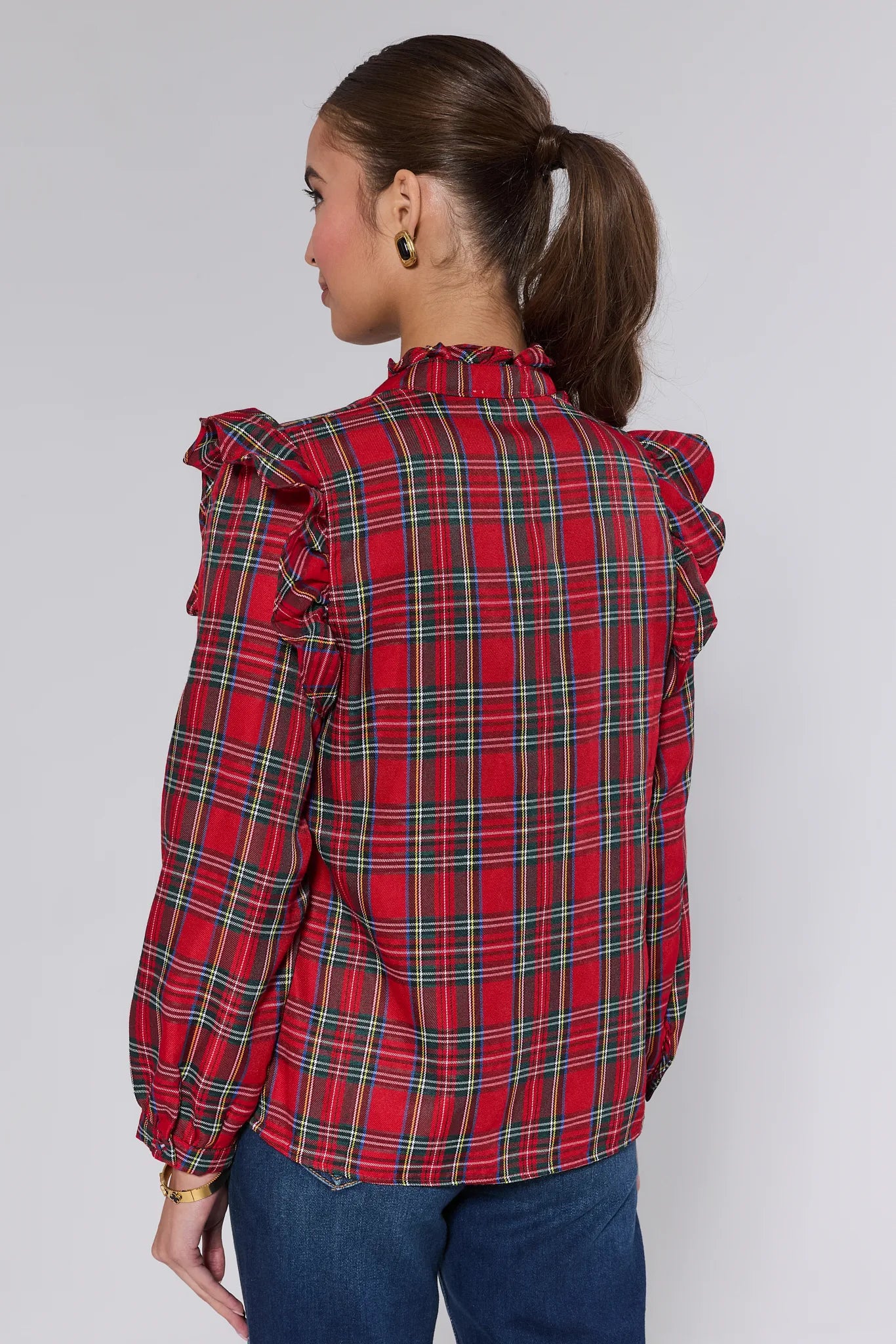 Woman wearing a Holly Plaid Button Up Top with ruffled sleeves and blue jeans, holding a silver clutch.