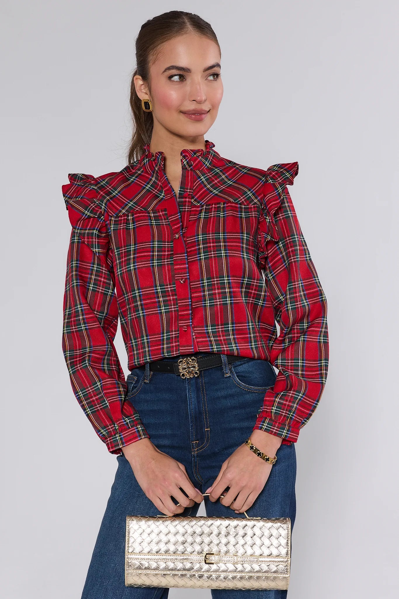 Woman wearing a Holly Plaid Button Up Top with ruffled sleeves and blue jeans, holding a silver clutch.