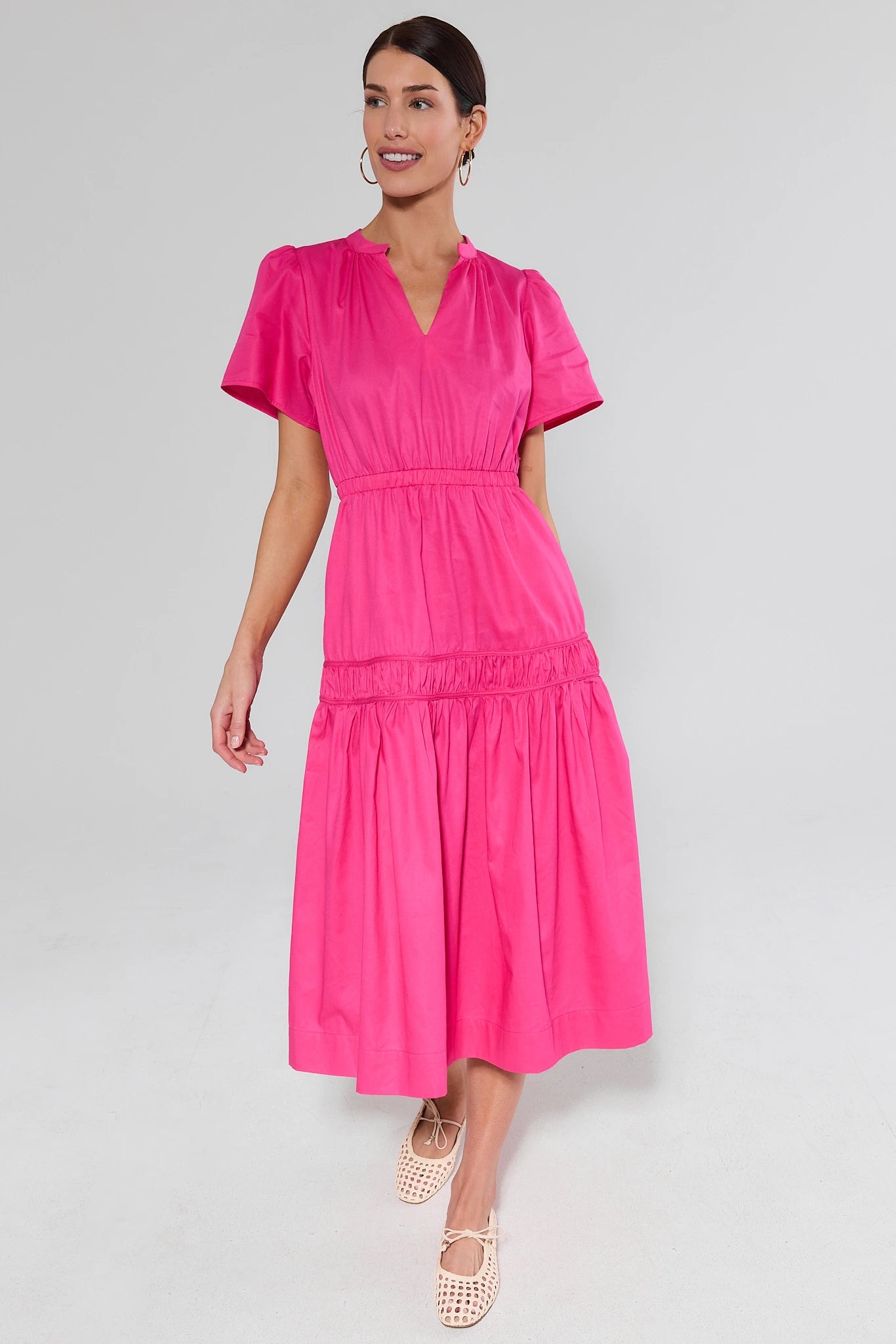 Woman wearing a bright pink dress and flats on a gray background