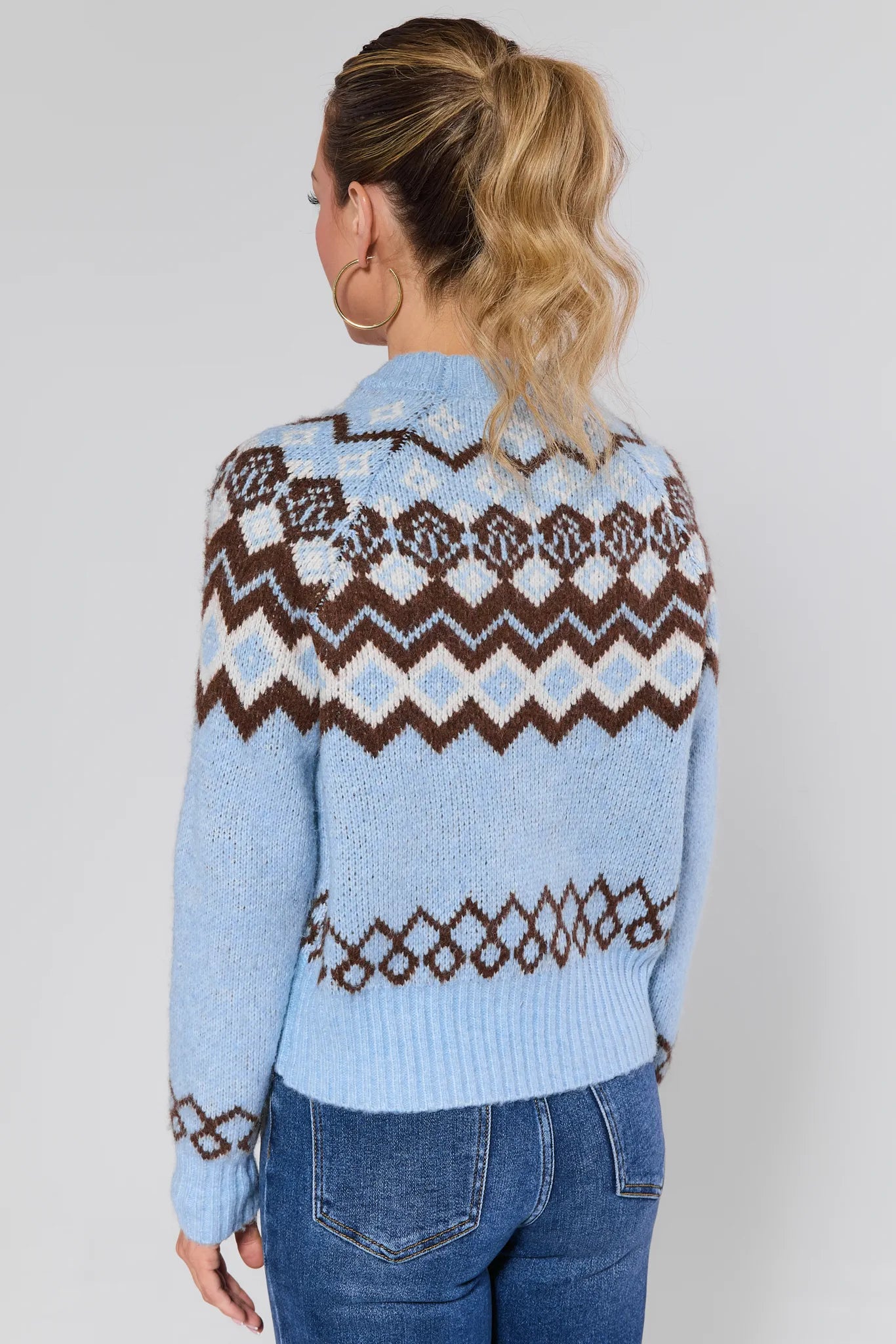 Woman wearing a blue astrid sweater with a pattern, standing against a plain background