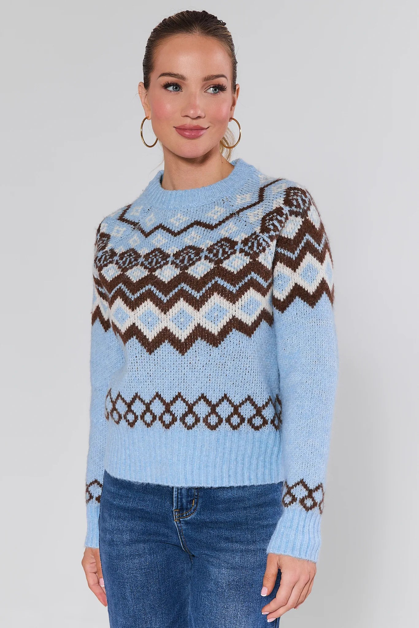 Woman wearing a blue astrid sweater with a pattern, standing against a plain background