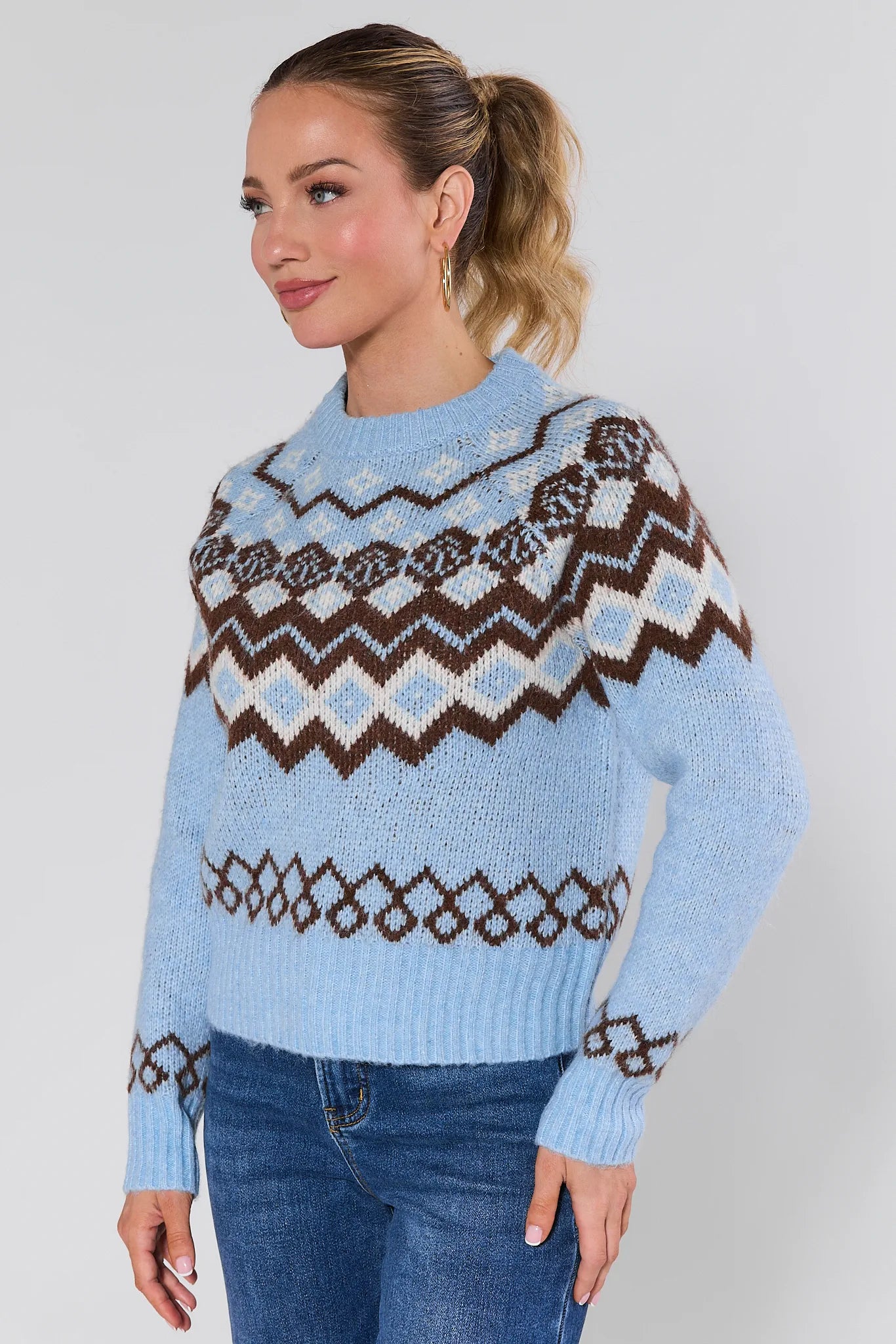 Woman wearing a blue astrid sweater with a pattern, standing against a plain background