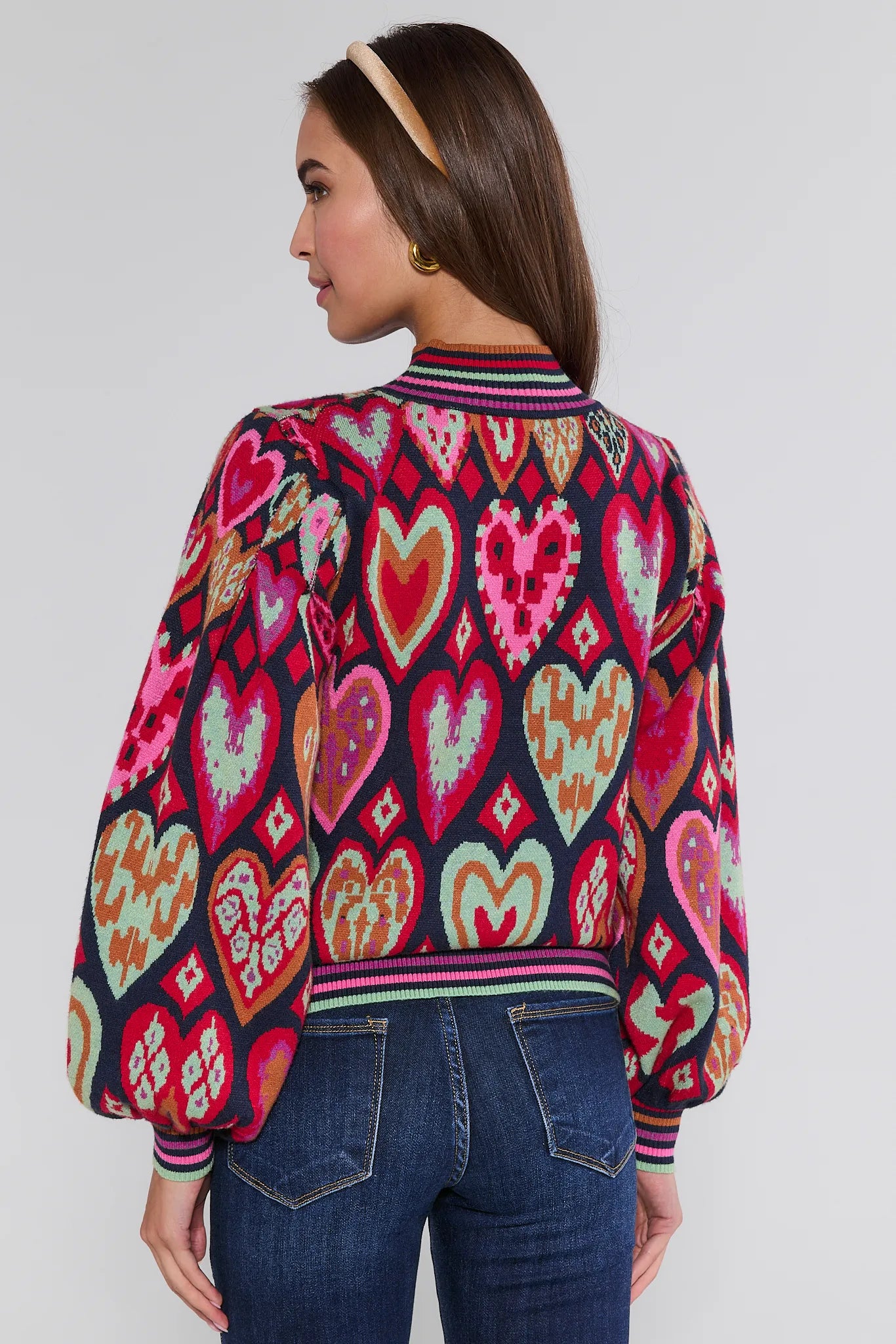 Woman wearing a colorful heart-patterned Maddie sweater against a white background