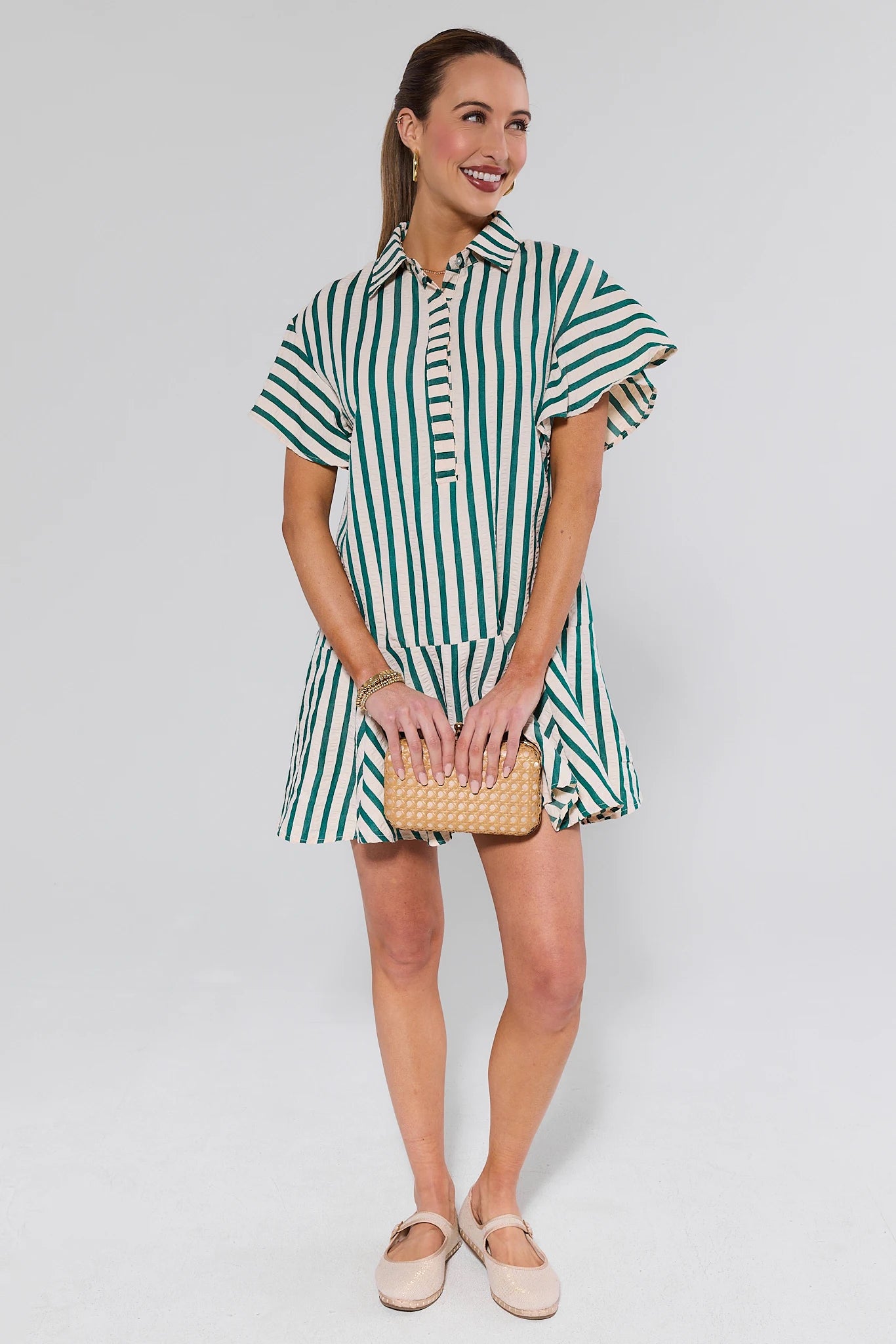 Woman wearing a green and white striped dress holding a woven bag on a plain background