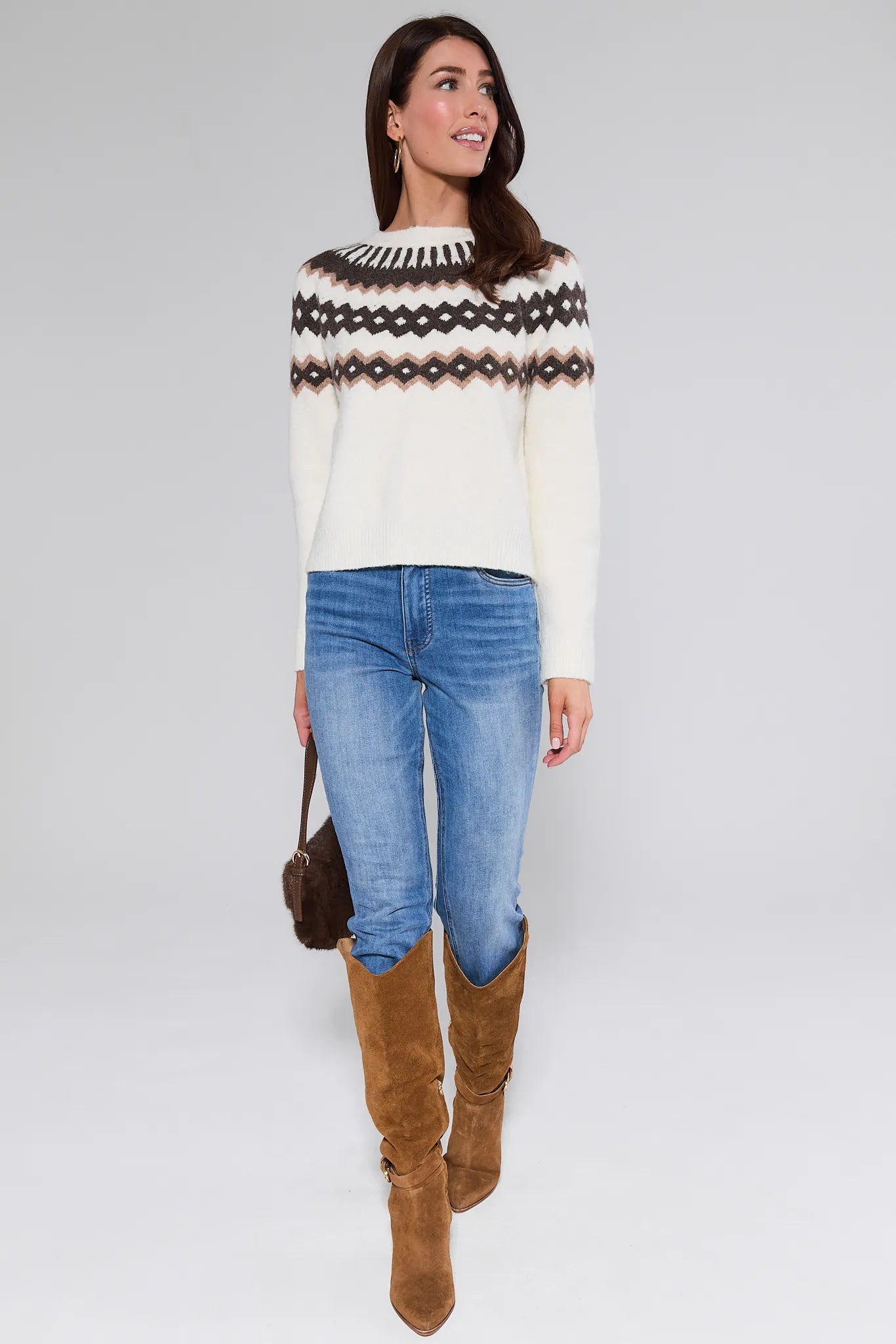 Woman wearing a patterned Marianne Sweater, jeans, and brown boots on a white background