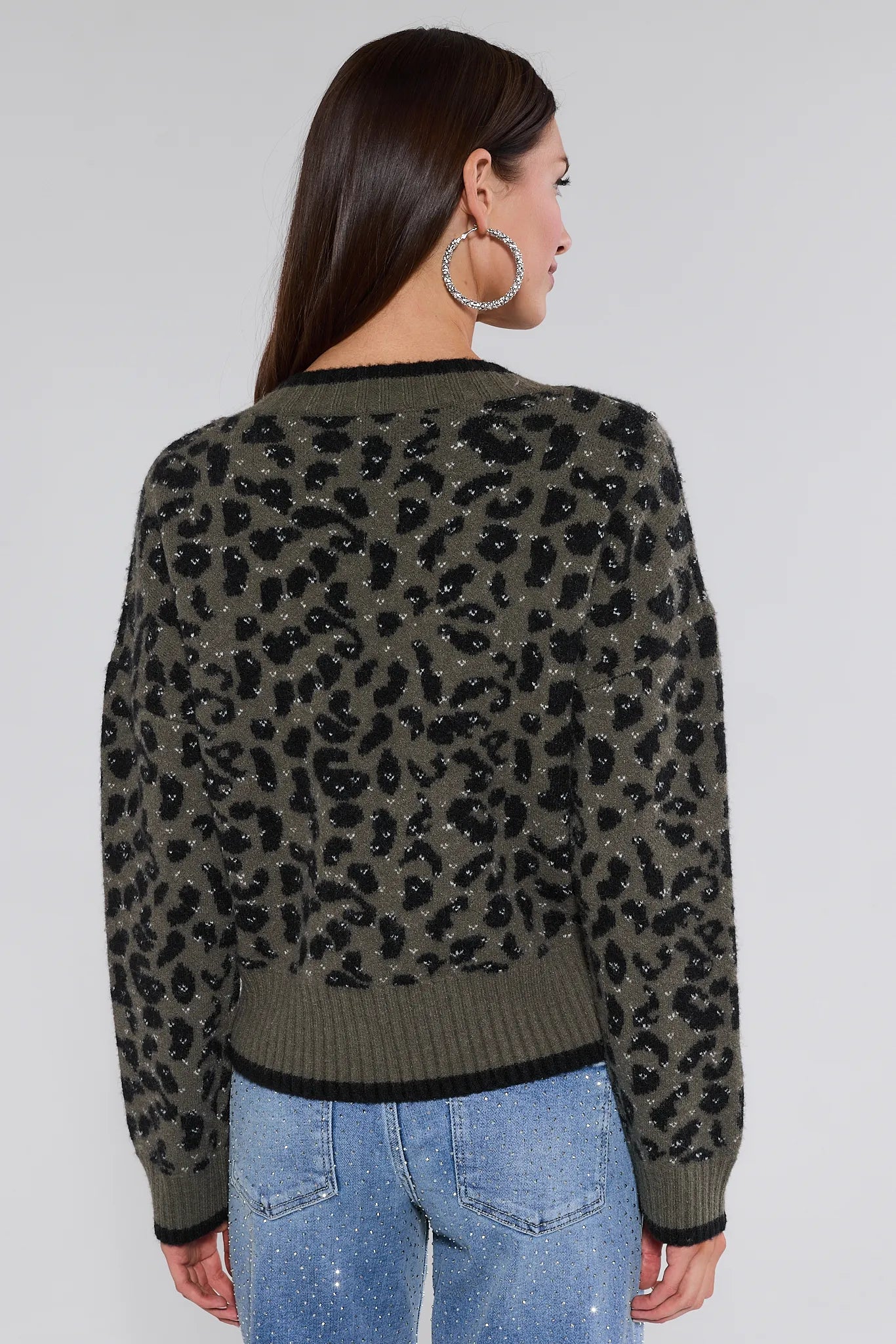Woman wearing a leopard print marcie sweater with sequins and blue jeans on a white background