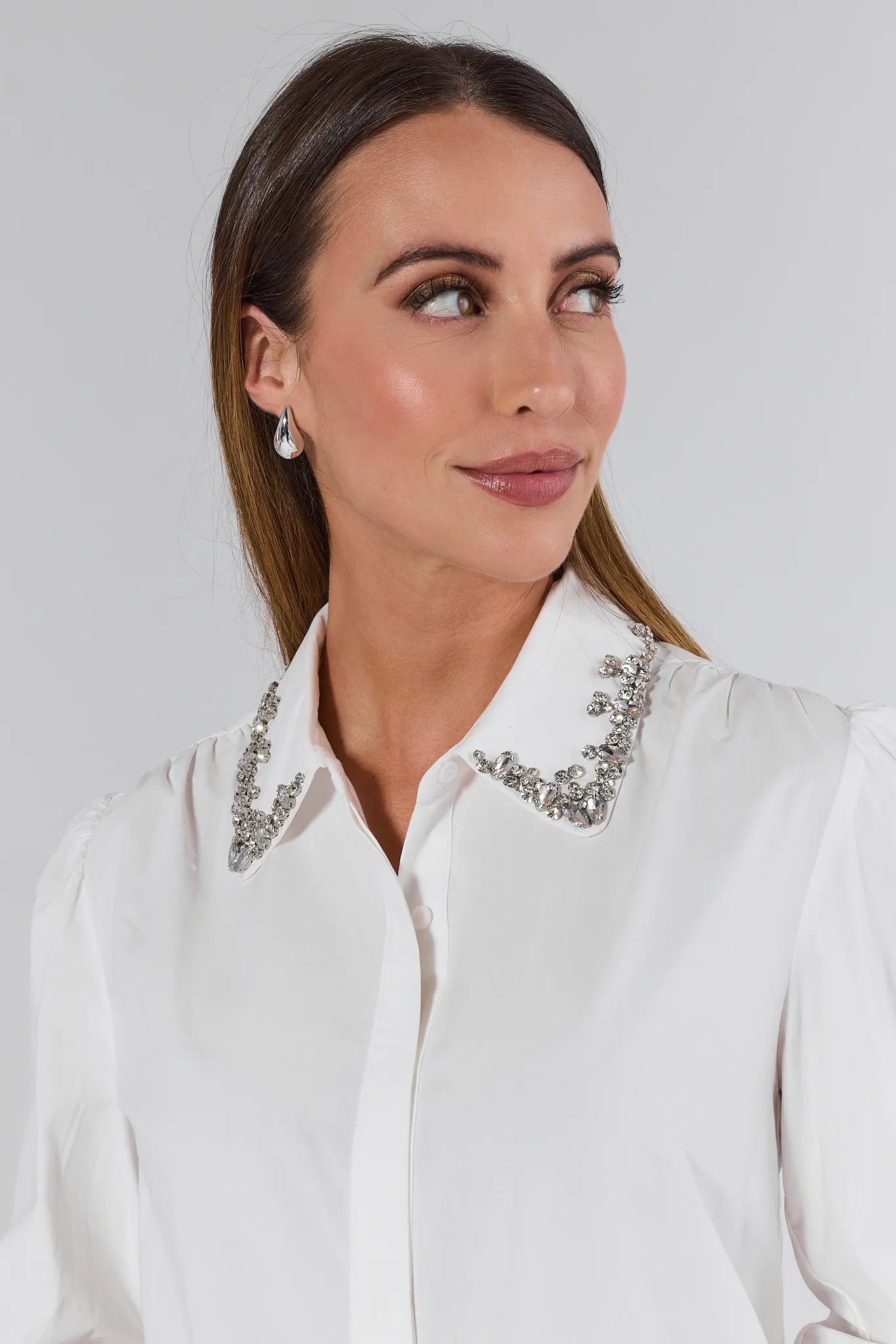 Woman wearing a white Celeste Top with embellishments and blue jeans on a plain background