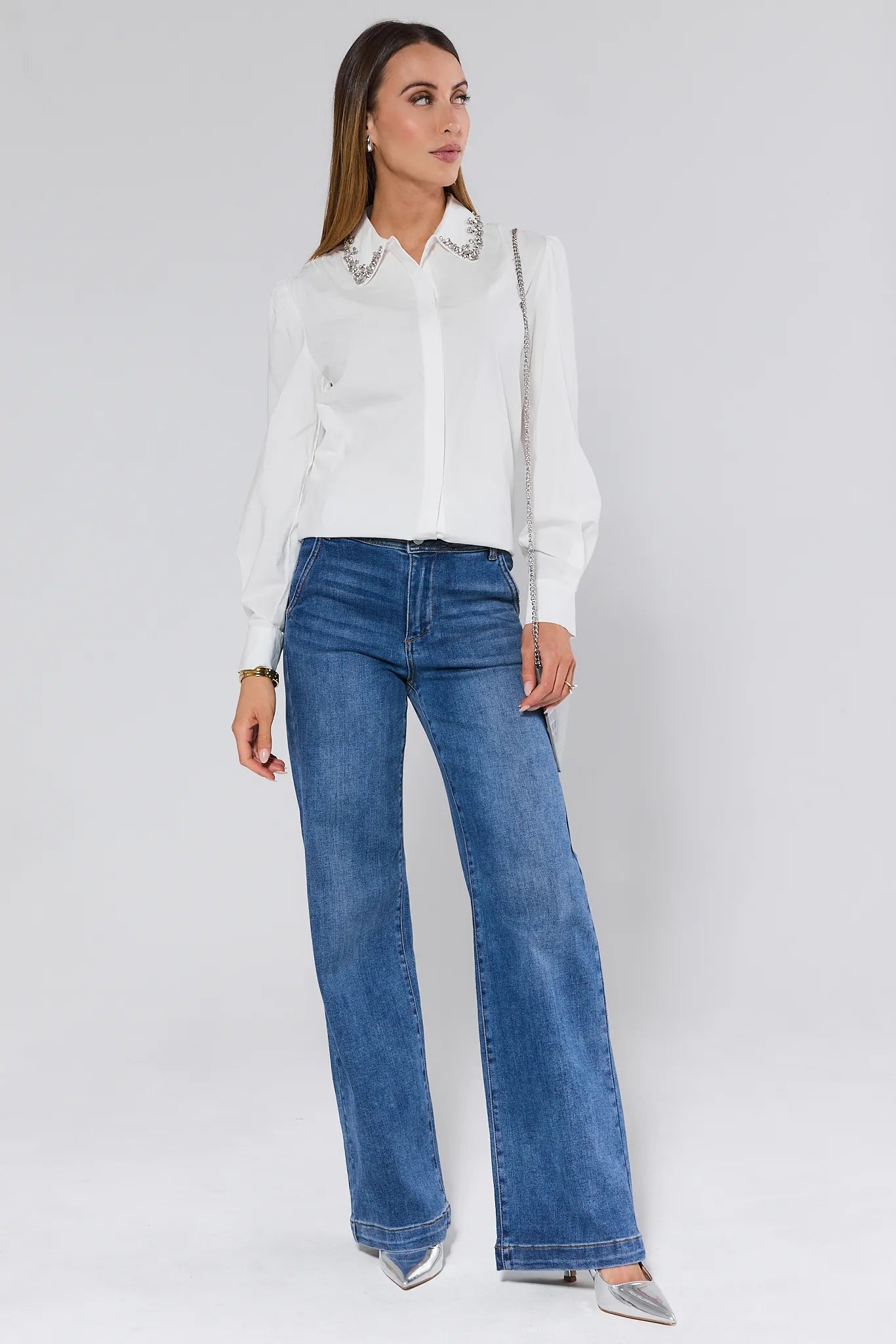 Woman wearing a white Celeste Top with embellishments and blue jeans on a plain background