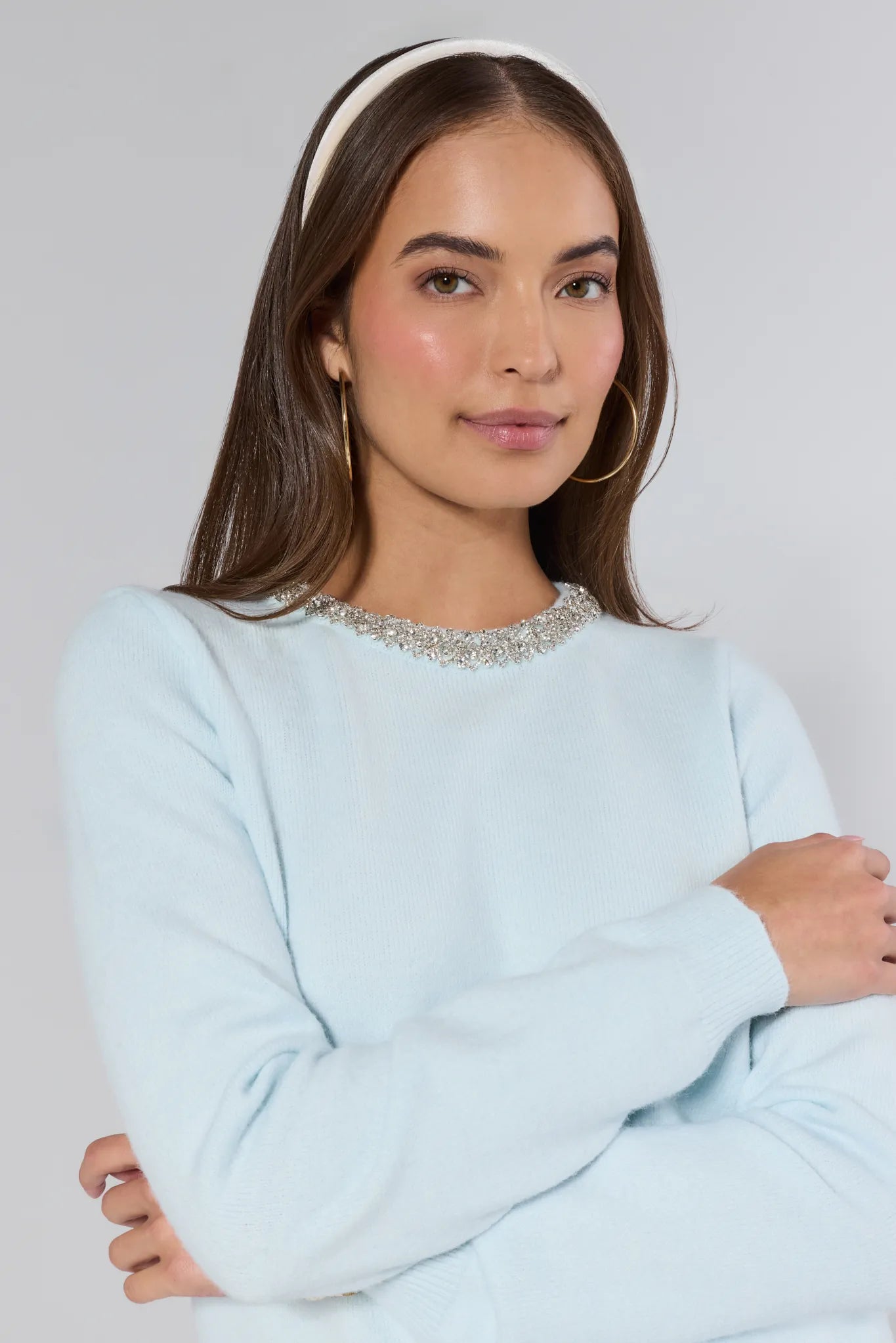 Woman wearing a light blue sweater with a decorative neckline against a plain background