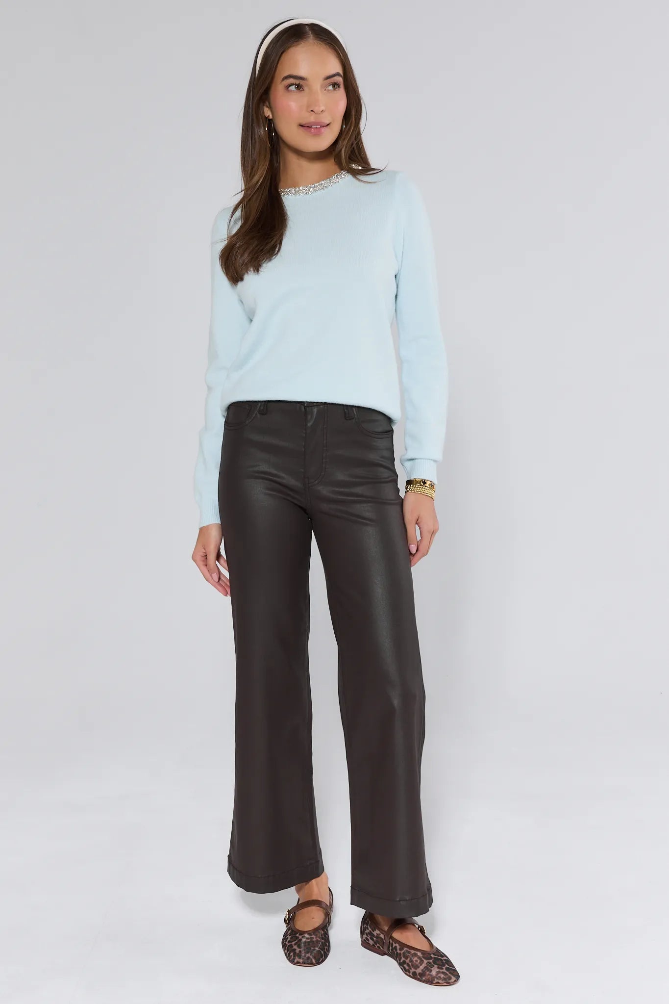 Woman wearing a light blue sweater and black leather pants on a white background