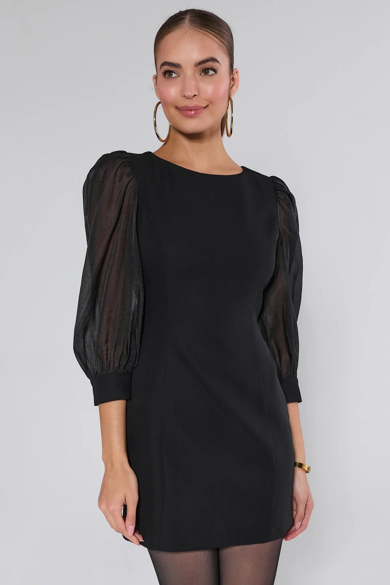 Woman wearing a black Veronica dress with sheer puff sleeves against a white background
