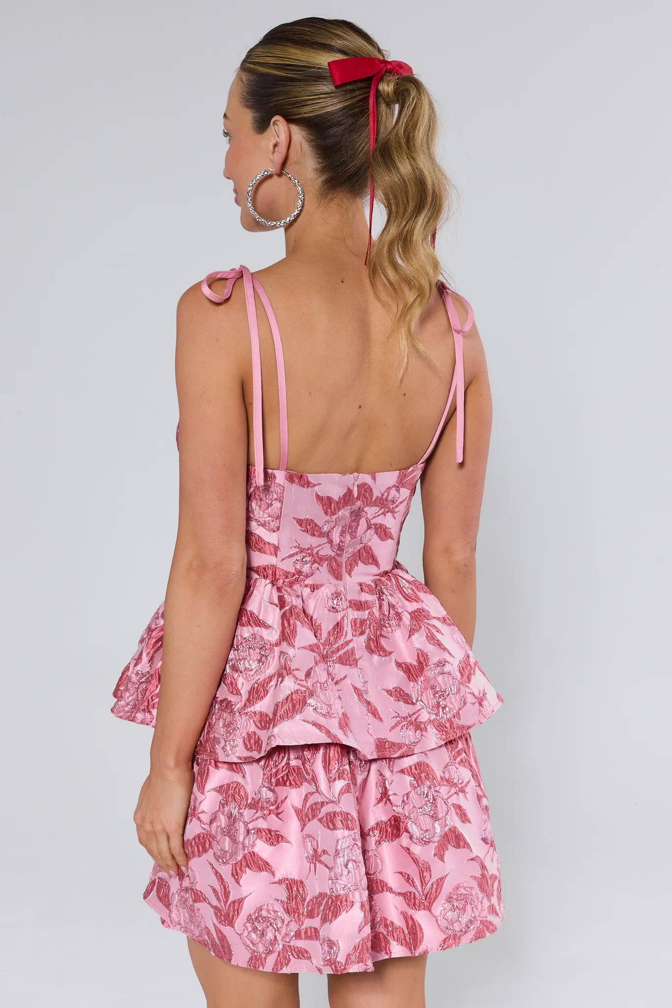 Woman wearing a pink floral dress with thin straps on a plain background