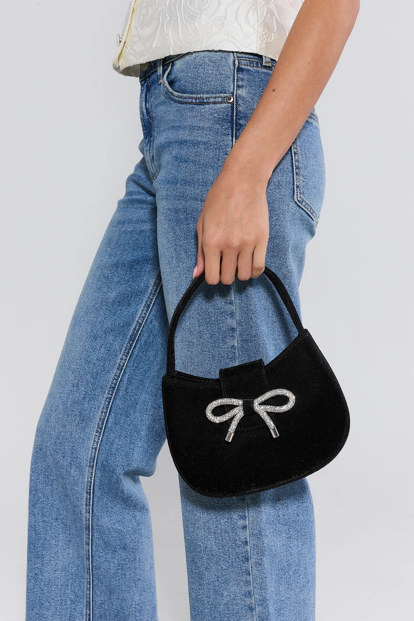 Person holding a Nina Black Velvet Bag, wearing blue jeans and a white top.