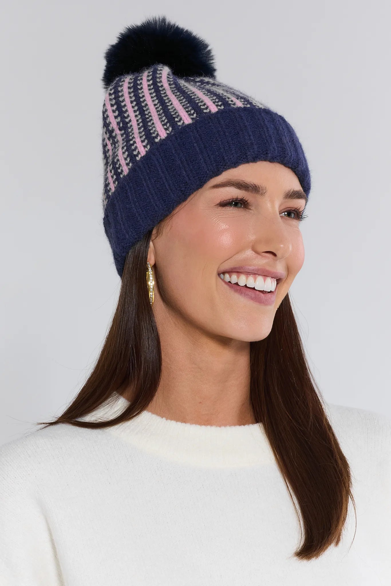 Woman wearing a blue and pink striped beanie with a pom-pom on a white background