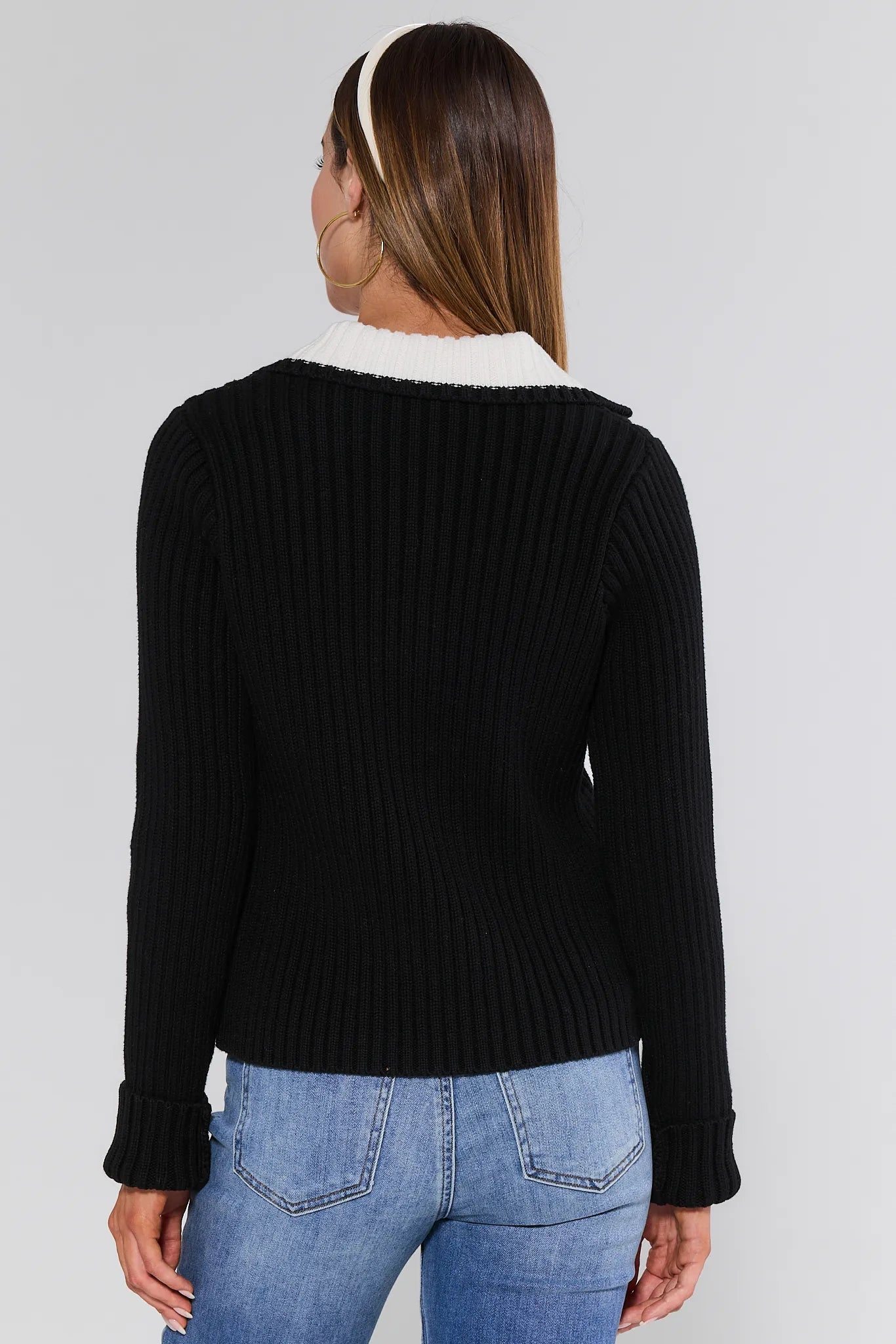 Person wearing a black ribbed Joey Sweater with white lining and blue jeans on a plain background