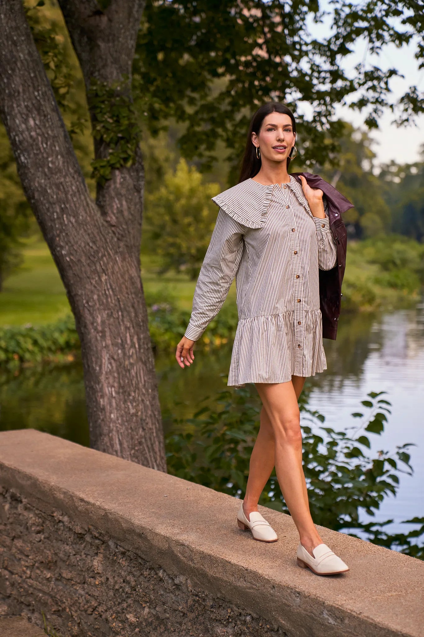 Woman in a light gray Berkley Dress standing by a tree and water body