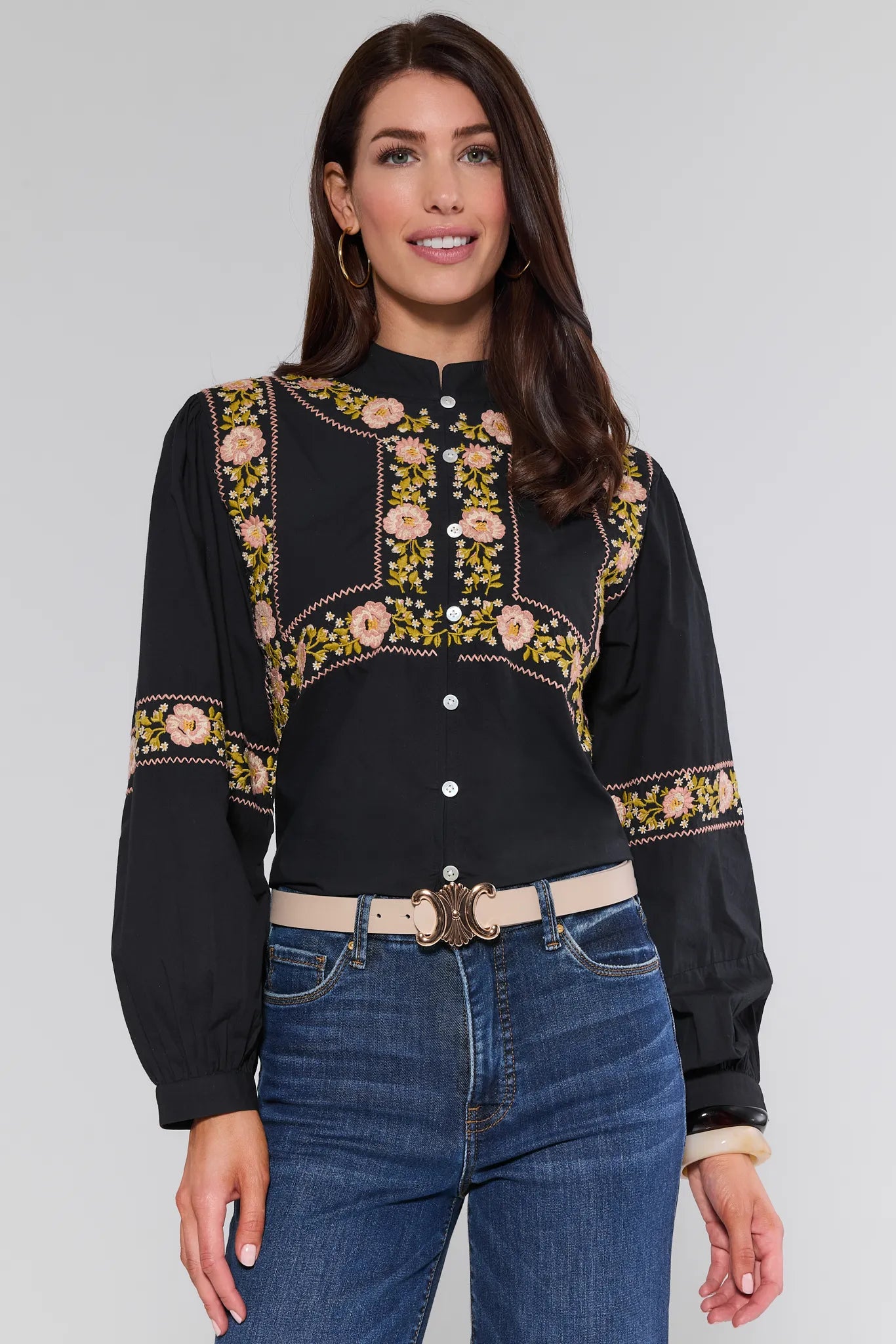 Woman wearing a black Selma Top with floral embroidery and blue jeans on a gray background