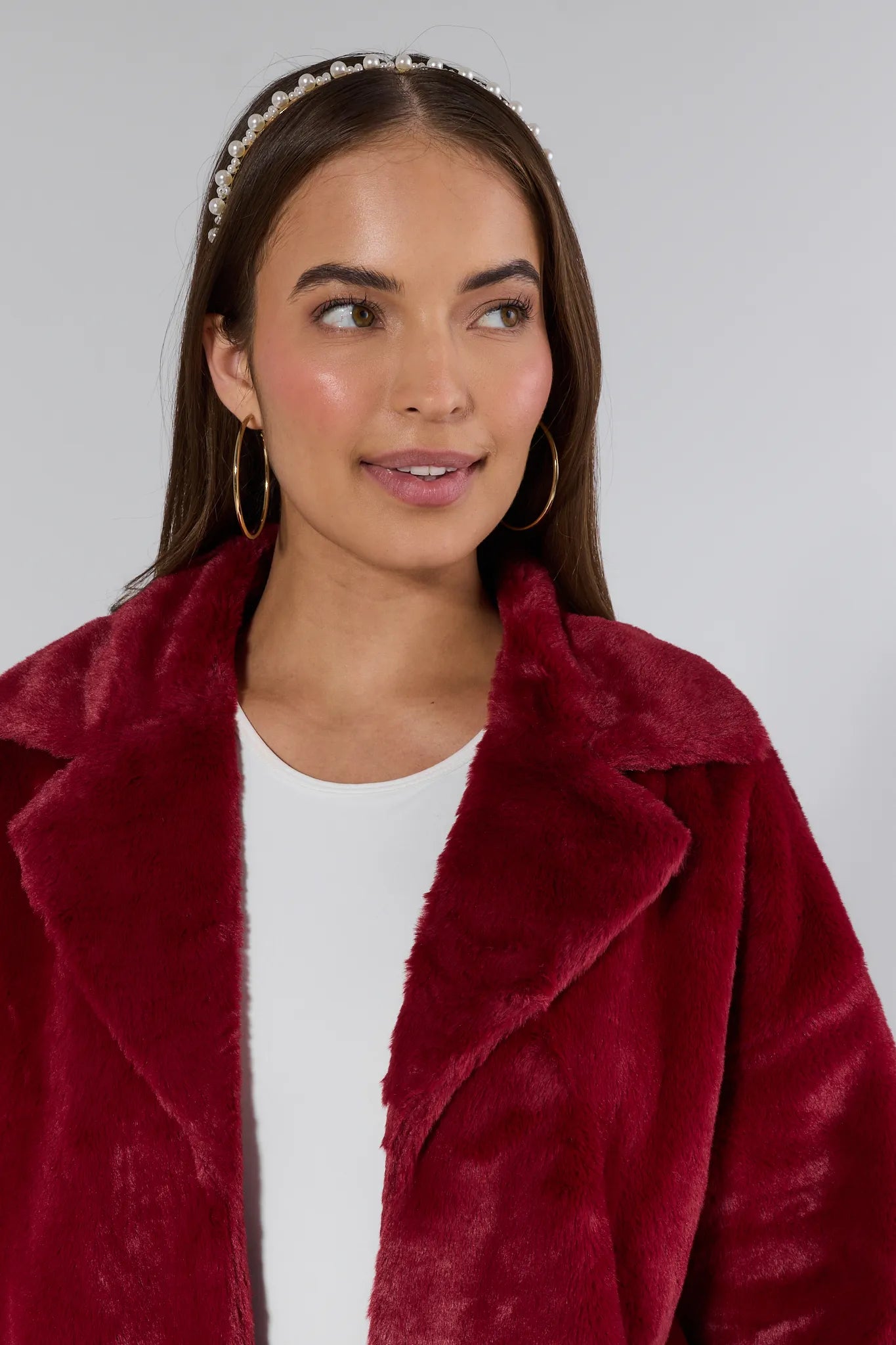 Woman wearing a burgundy faux fur coat with a plain background