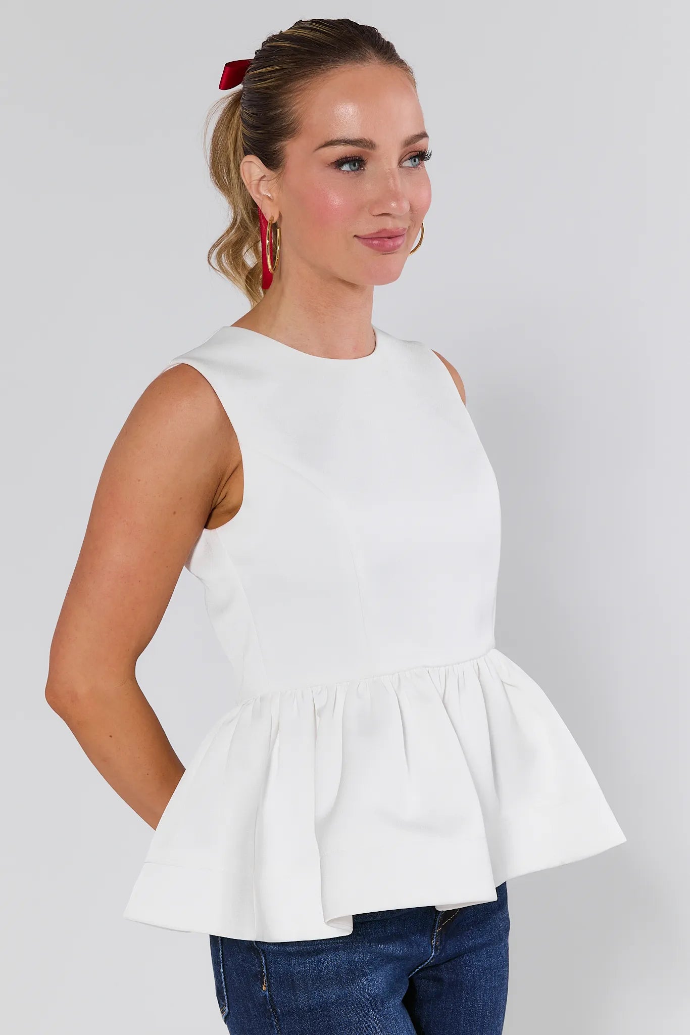 Woman wearing a Blakey Ivory Peplum Top and blue jeans against a plain background