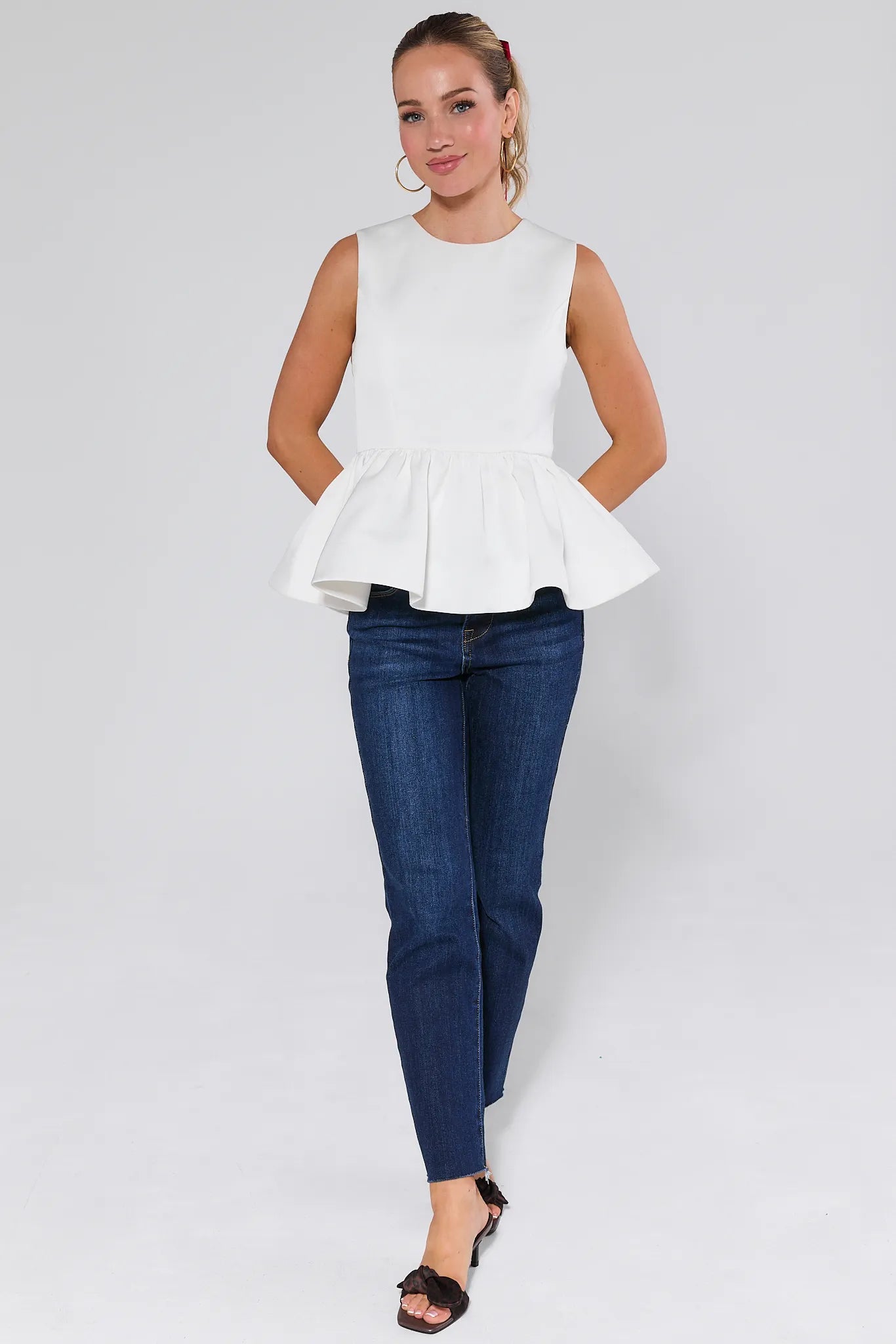 Woman wearing a Blakey Ivory Peplum Top and blue jeans against a plain background