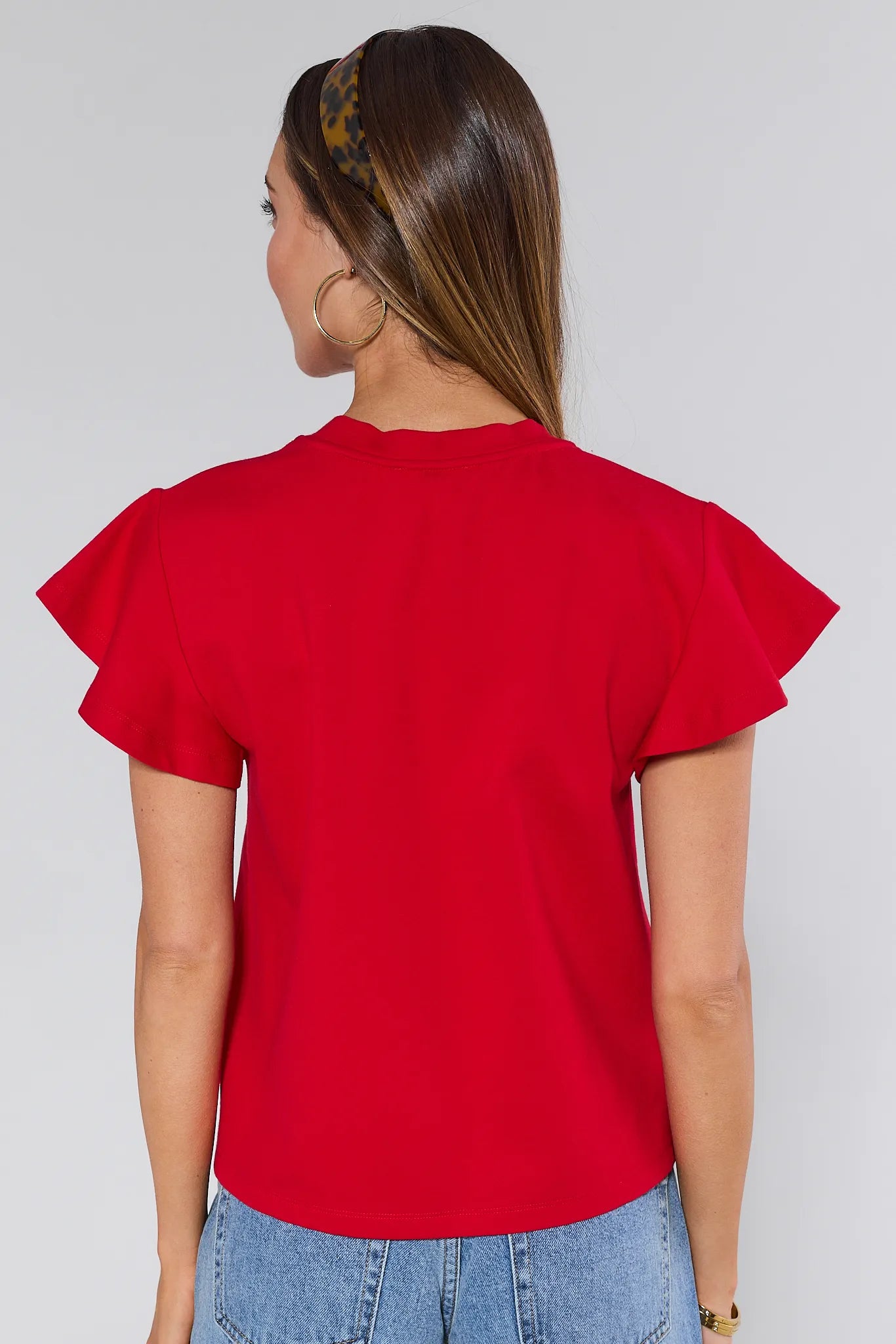 Woman wearing a red Elodie top and blue jeans against a white background