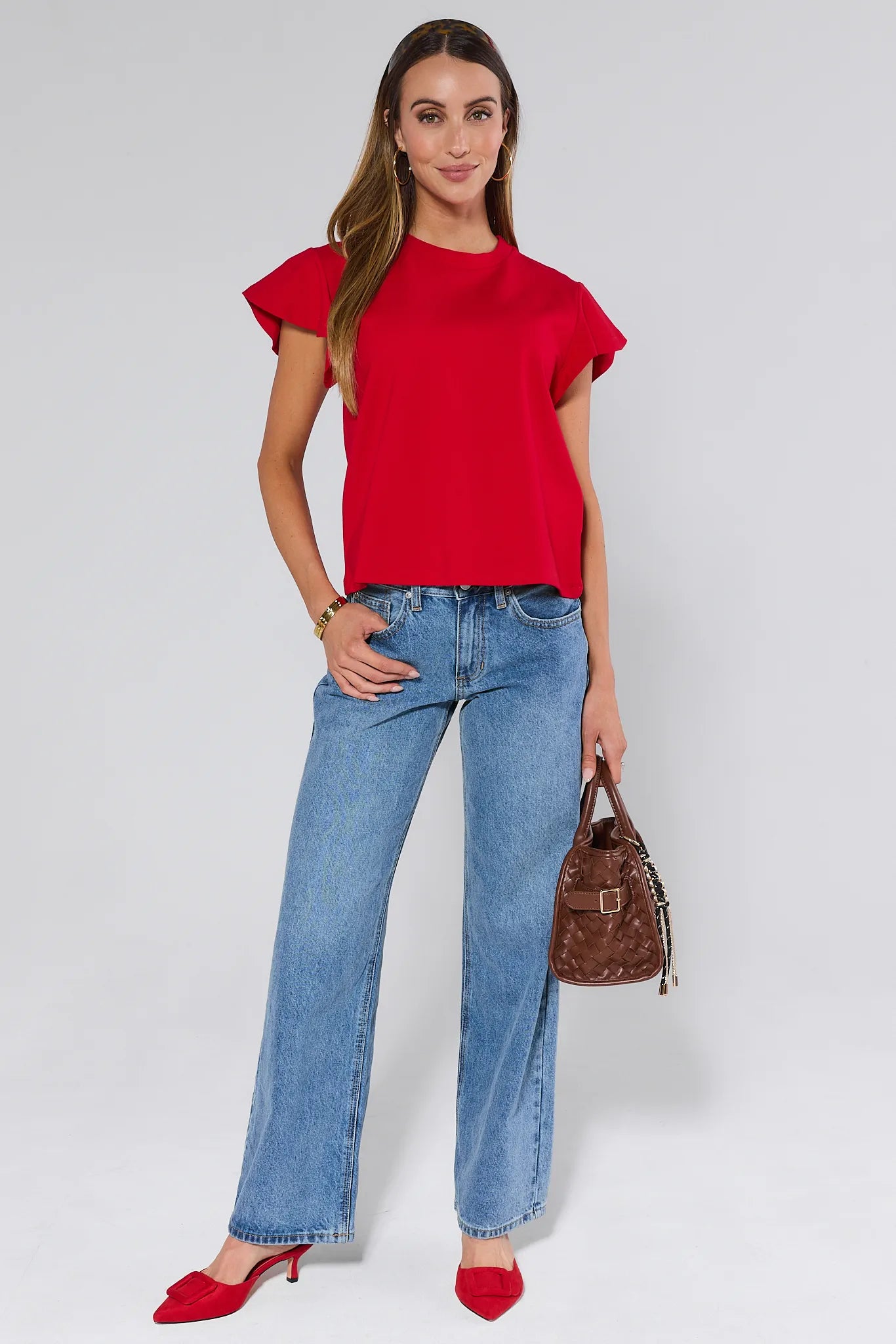 Woman wearing a red Elodie top and blue jeans against a white background