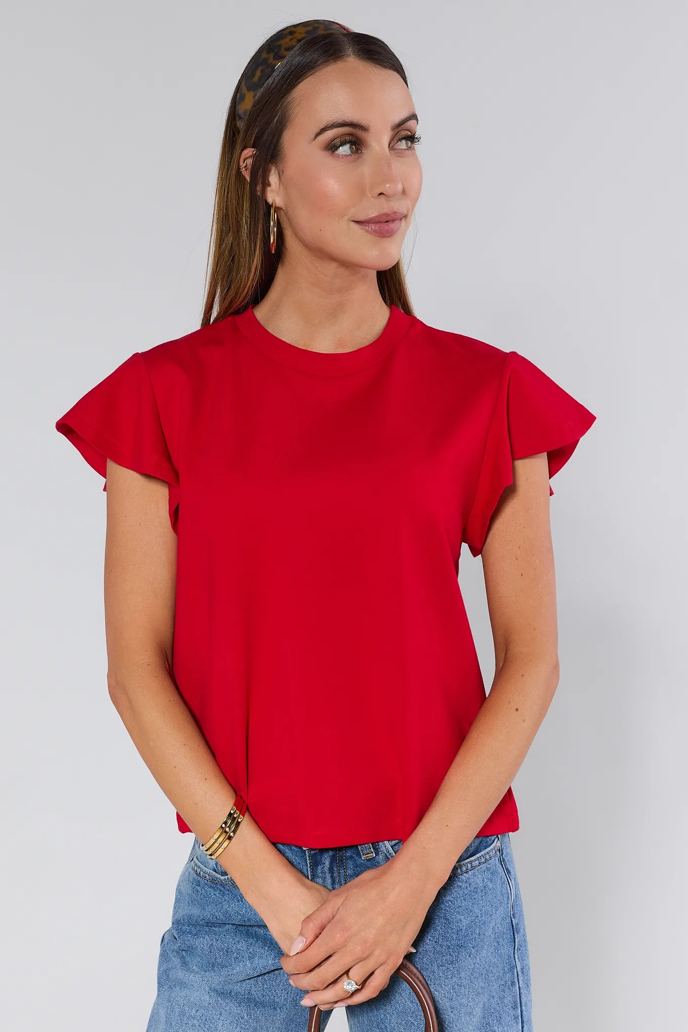 Woman wearing a red Elodie top and blue jeans against a white background