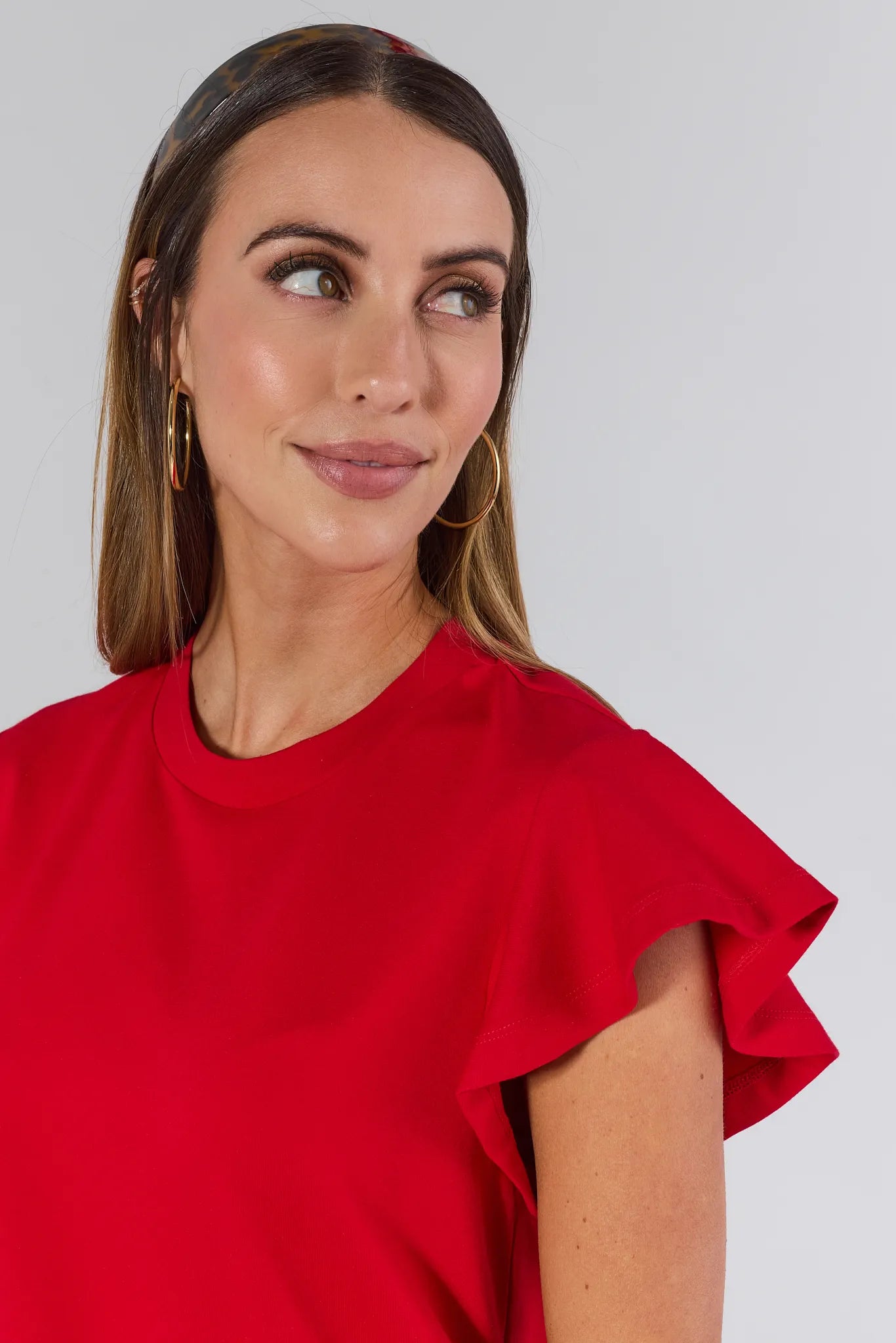 Woman wearing a red Elodie top and blue jeans against a white background