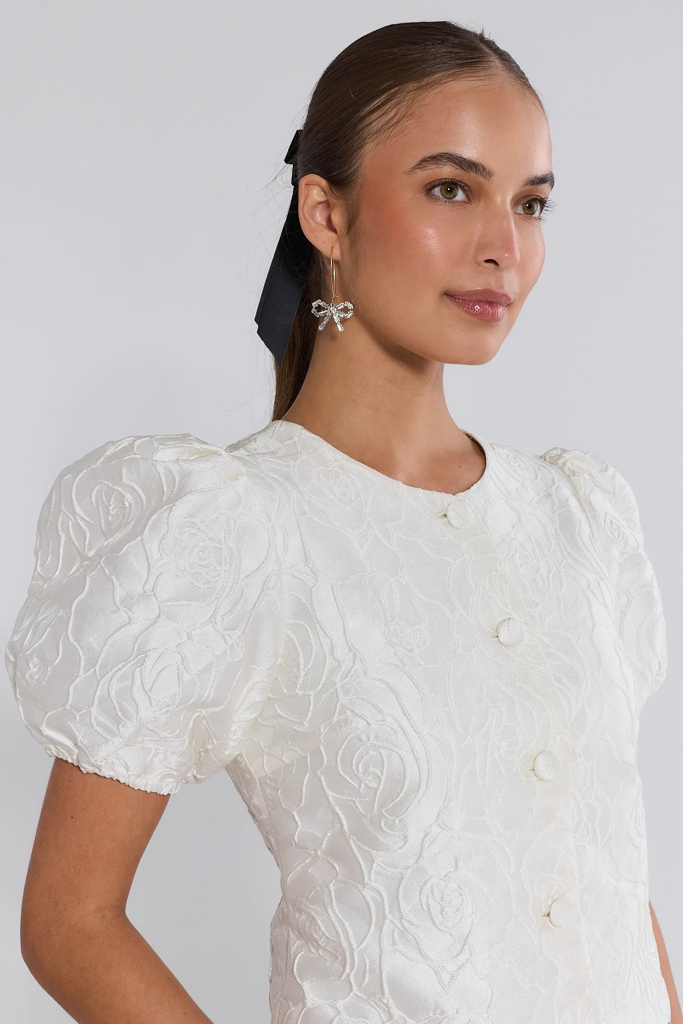 Woman wearing a white embroidered dress against a plain background