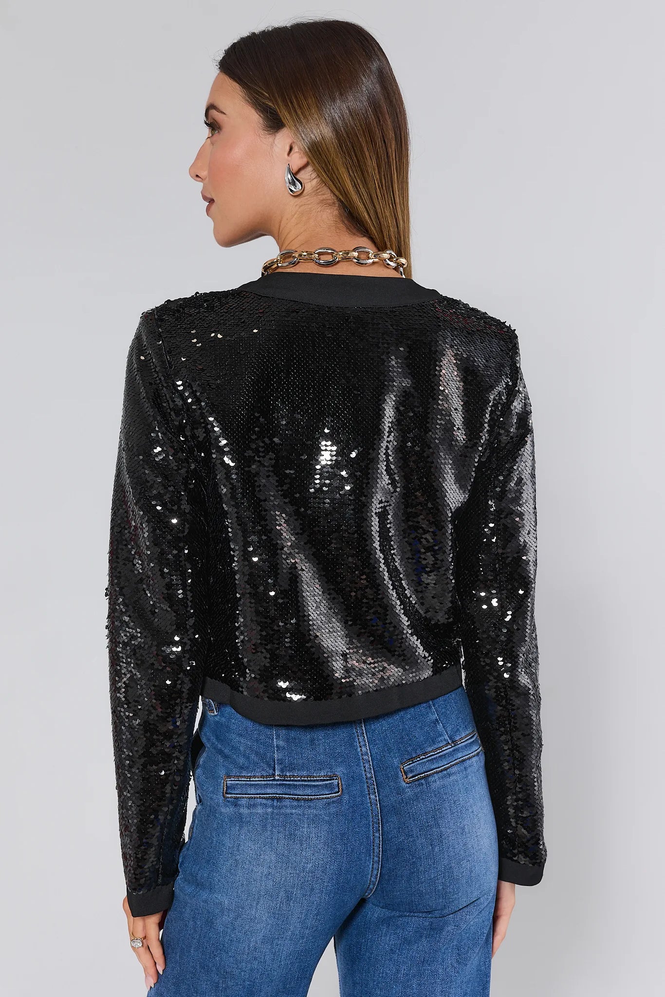 Person wearing a Wren Black Sequin Jacket and blue jeans on a plain background