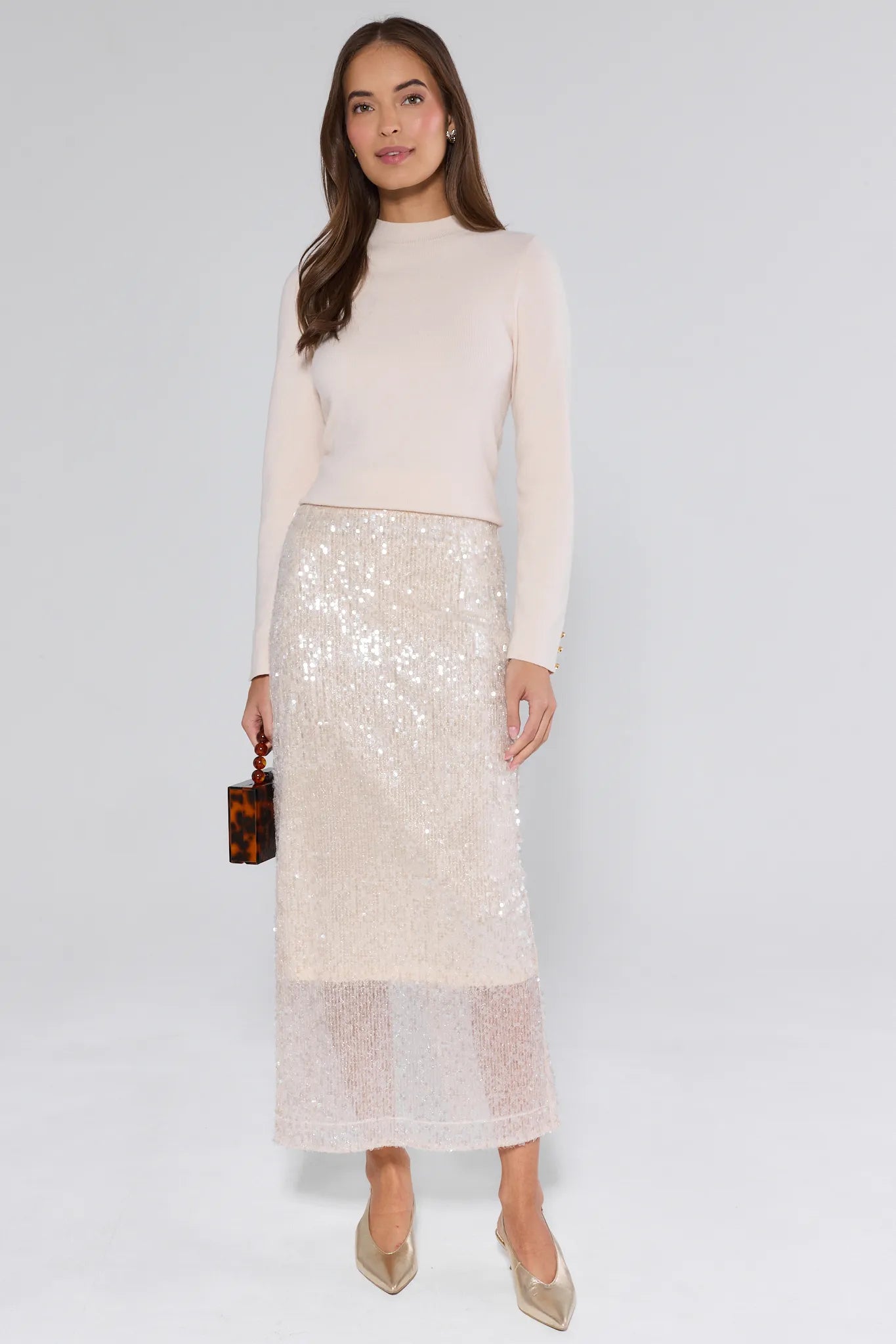 Woman wearing a cream sequin skirt and sweater on a white background