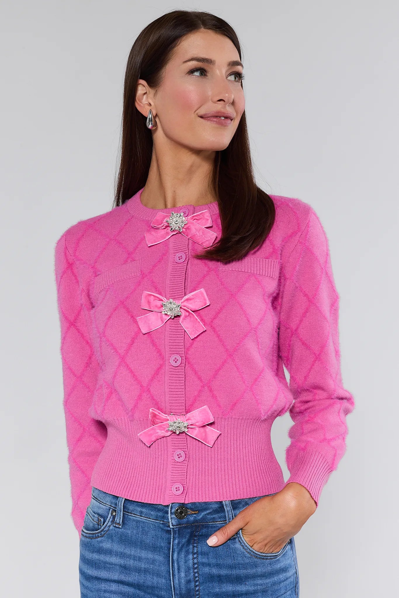 Woman wearing a Emily Pink Bow Cardigan with decorative bows and buttons on a plain background