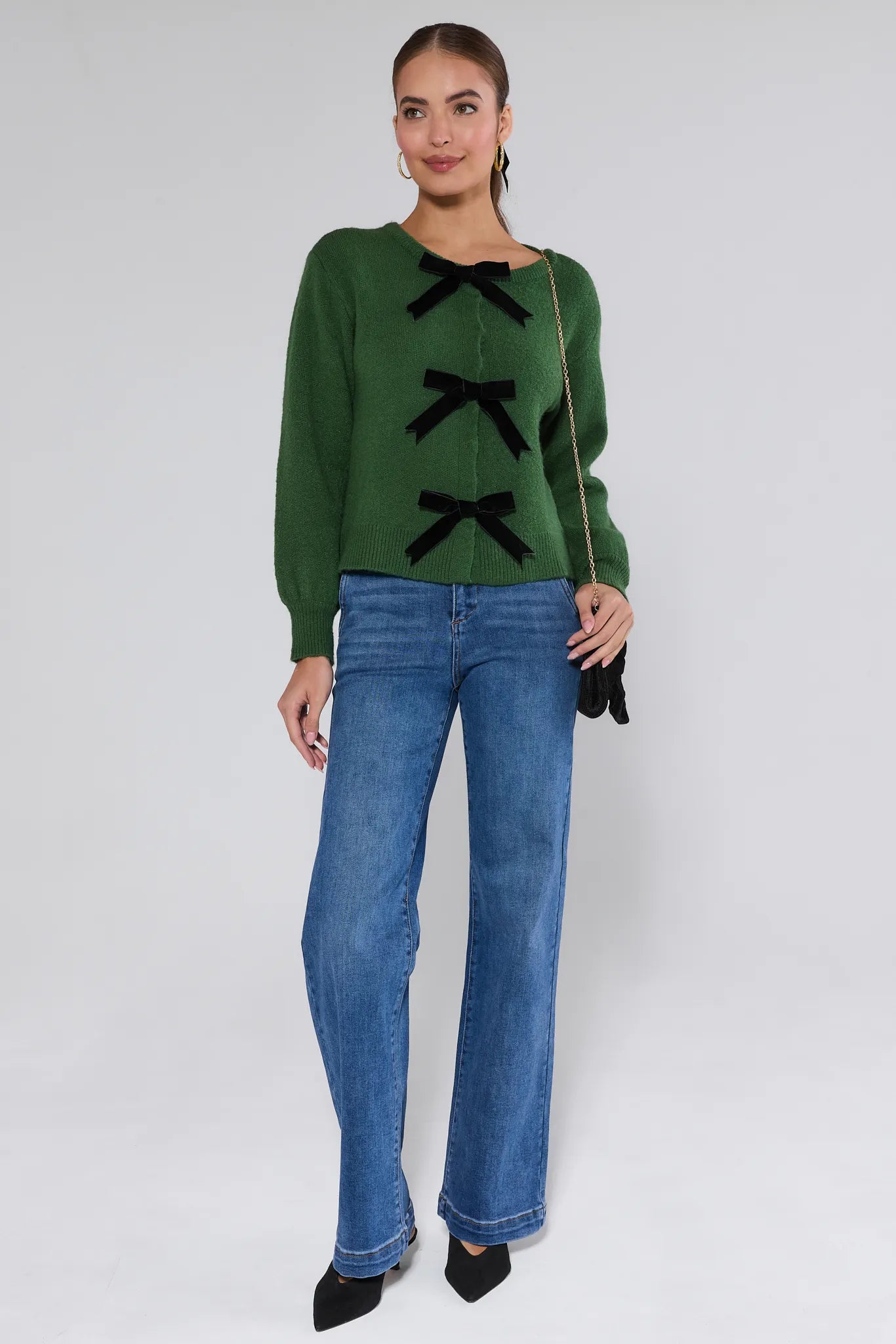 Woman wearing a Everly Green Bow Knit Sweater with black bows and blue jeans against a white background