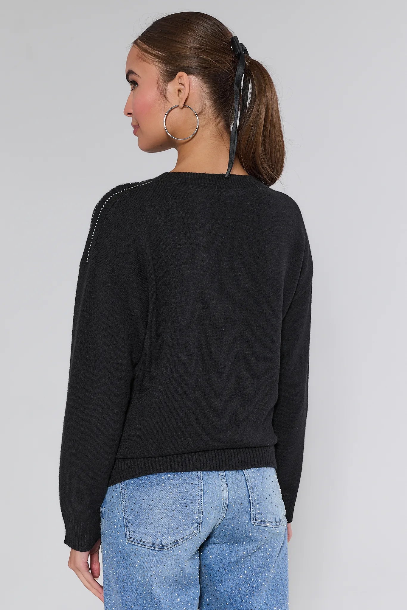 Woman wearing a Sondra Black Embellished Sweater with decorative elements and blue jeans on a white background
