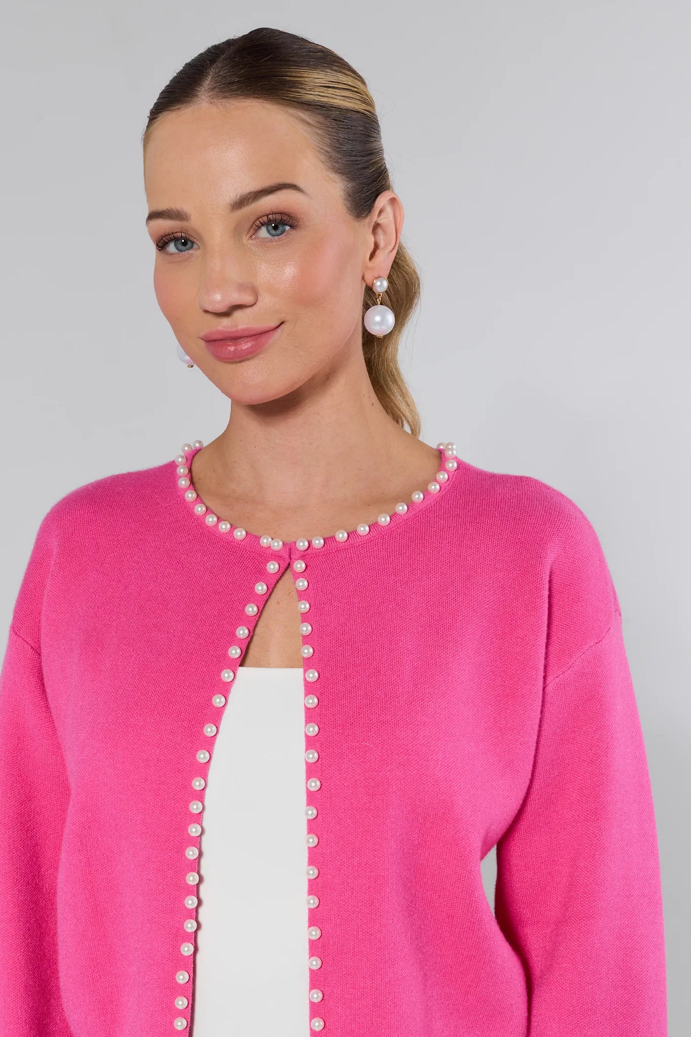 Woman wearing a pink cardigan with pearl buttons on a gray background