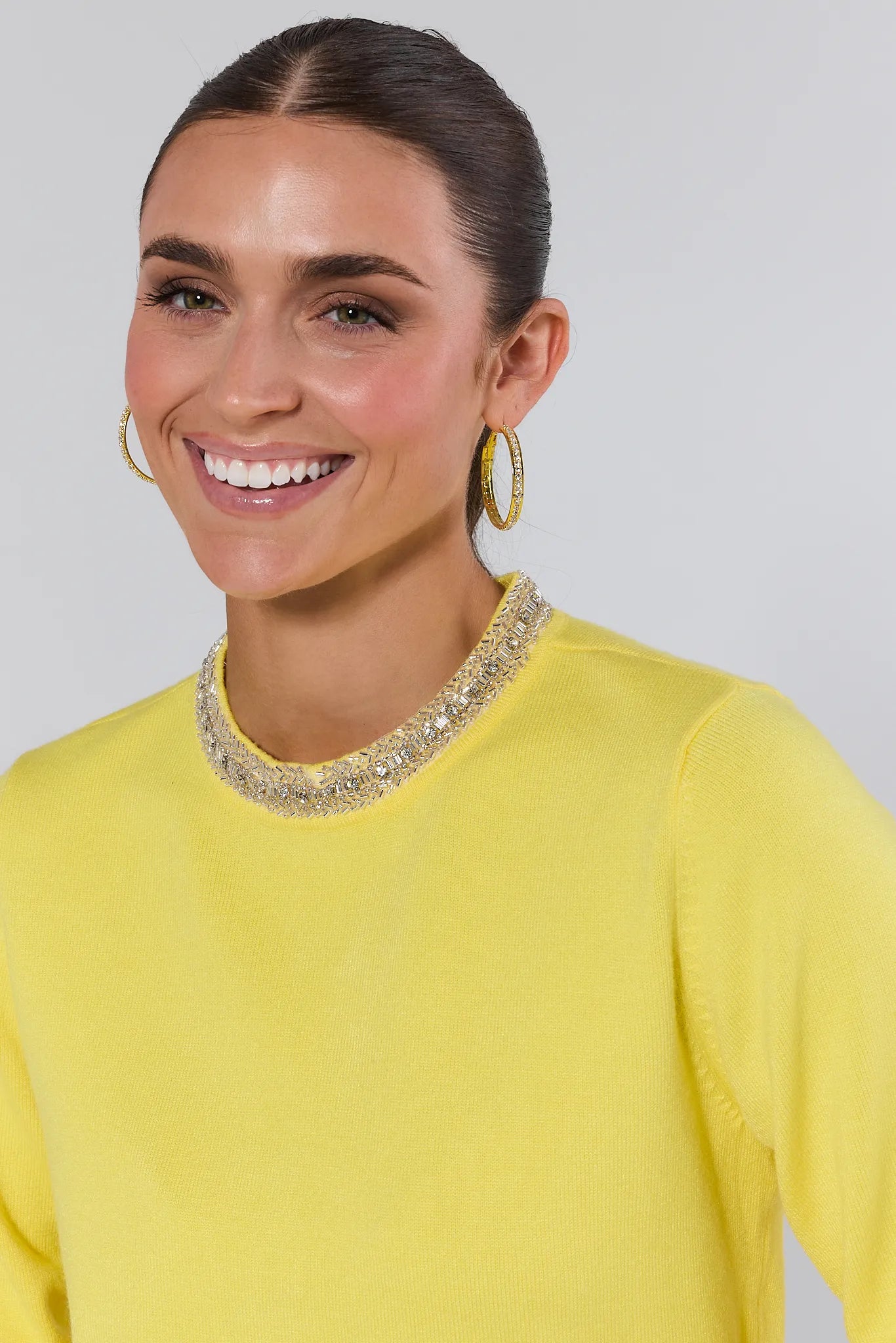 Woman wearing a yellow victoria sweater and blue jeans against a plain background