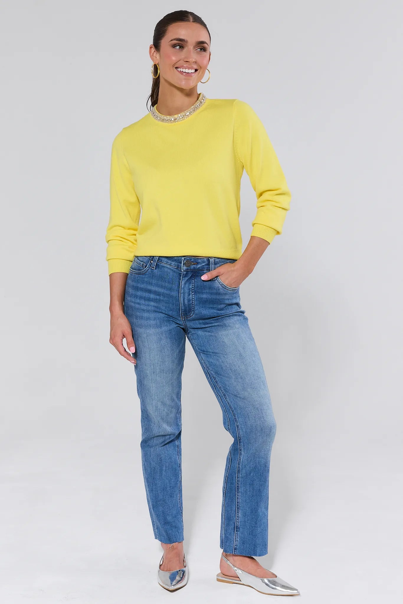 Woman wearing a yellow victoria sweater and blue jeans against a plain background