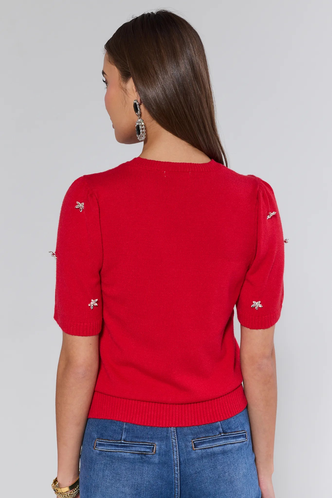 Woman wearing a red sweater with small white designs on a plain background