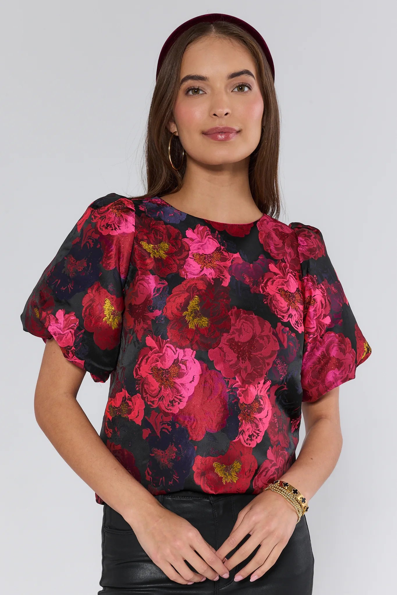 Woman wearing a floral Ruby Top with pink and red flowers on a plain background