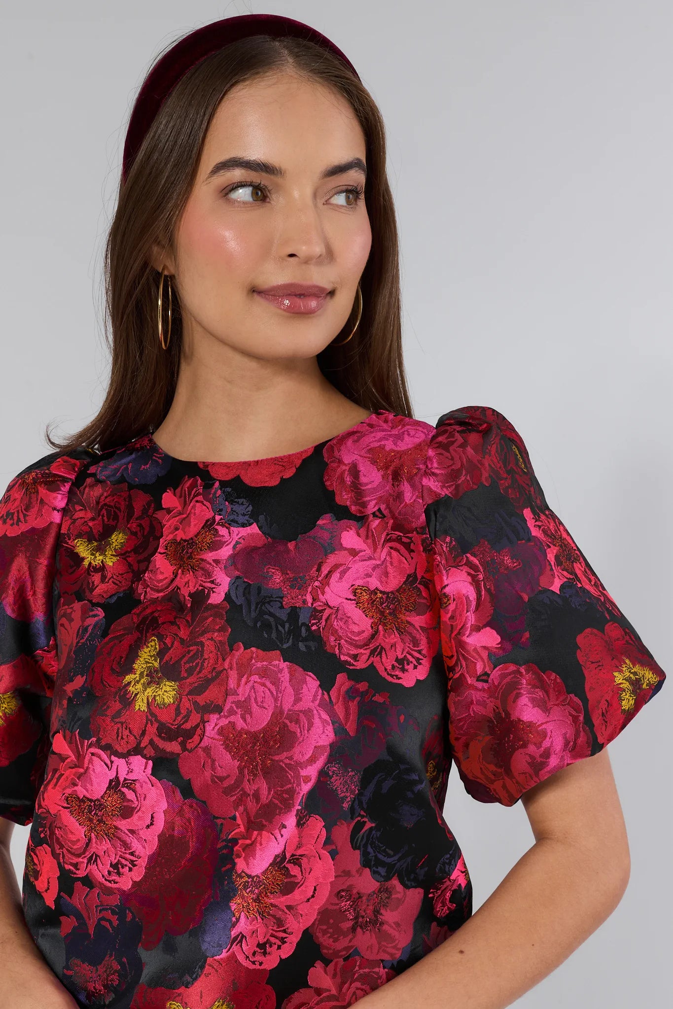 Woman wearing a floral Ruby Top with pink and red flowers on a plain background